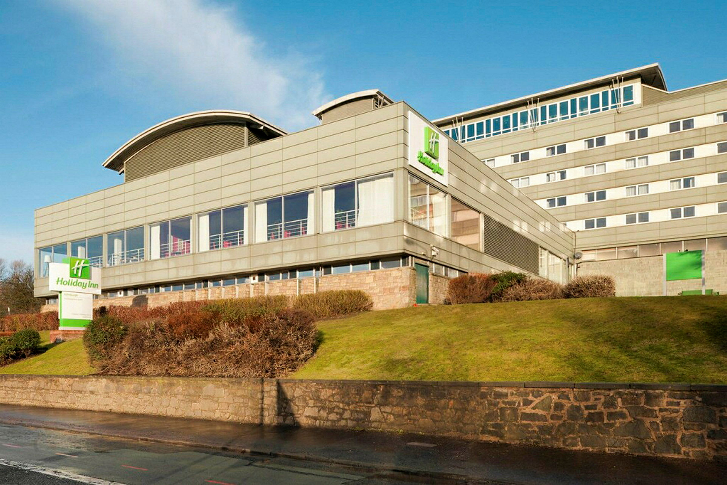 Holiday Inn-hotel i en moderne bygning omgivet af græsplæne og buske. (AI-genereret tekst)