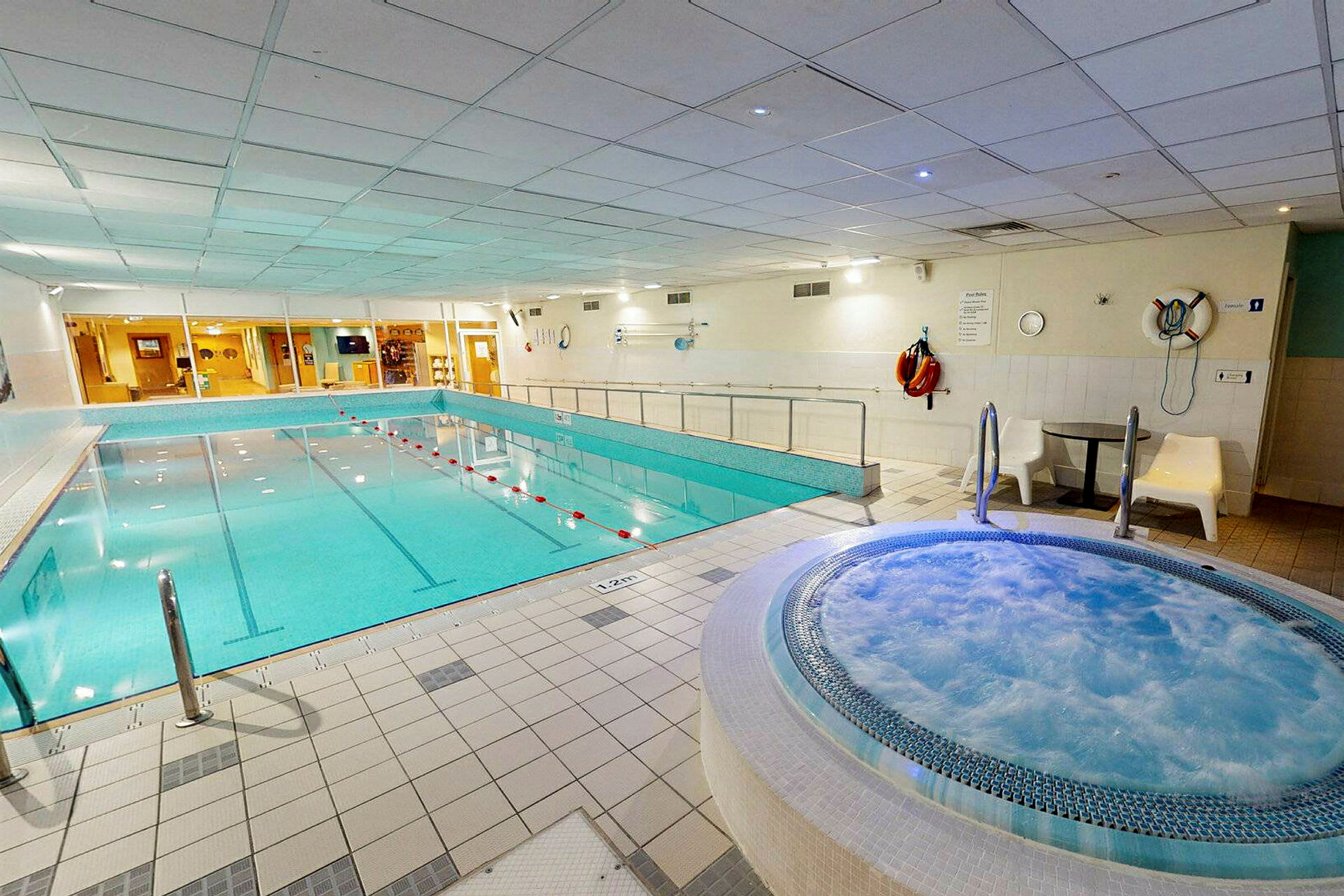 Indendørs poolområde med en stor pool og et boblebad. (AI-genereret tekst)
