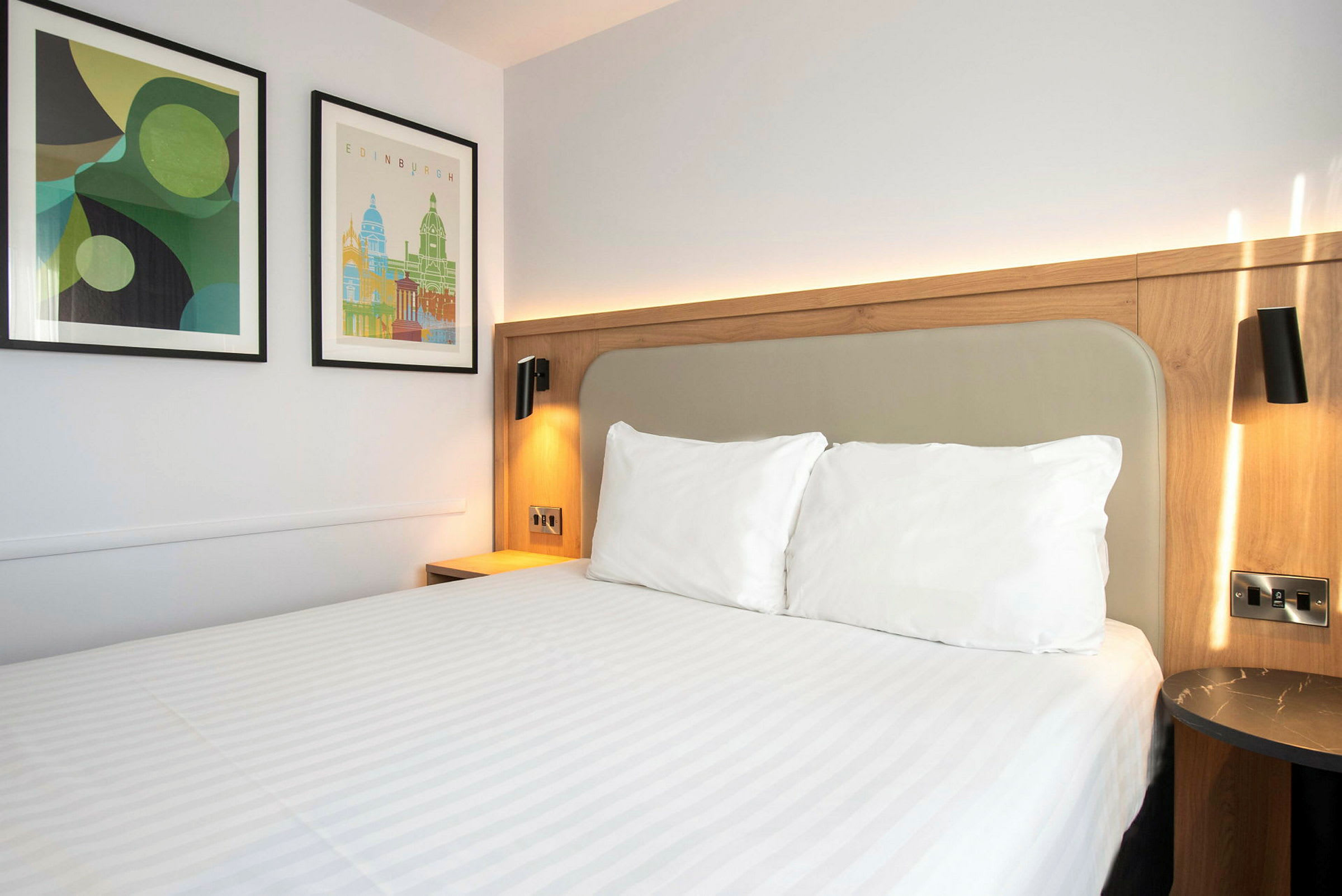 En hotelseng med hvidt sengetøj og to billeder på væggen. (AI-genereret tekst)