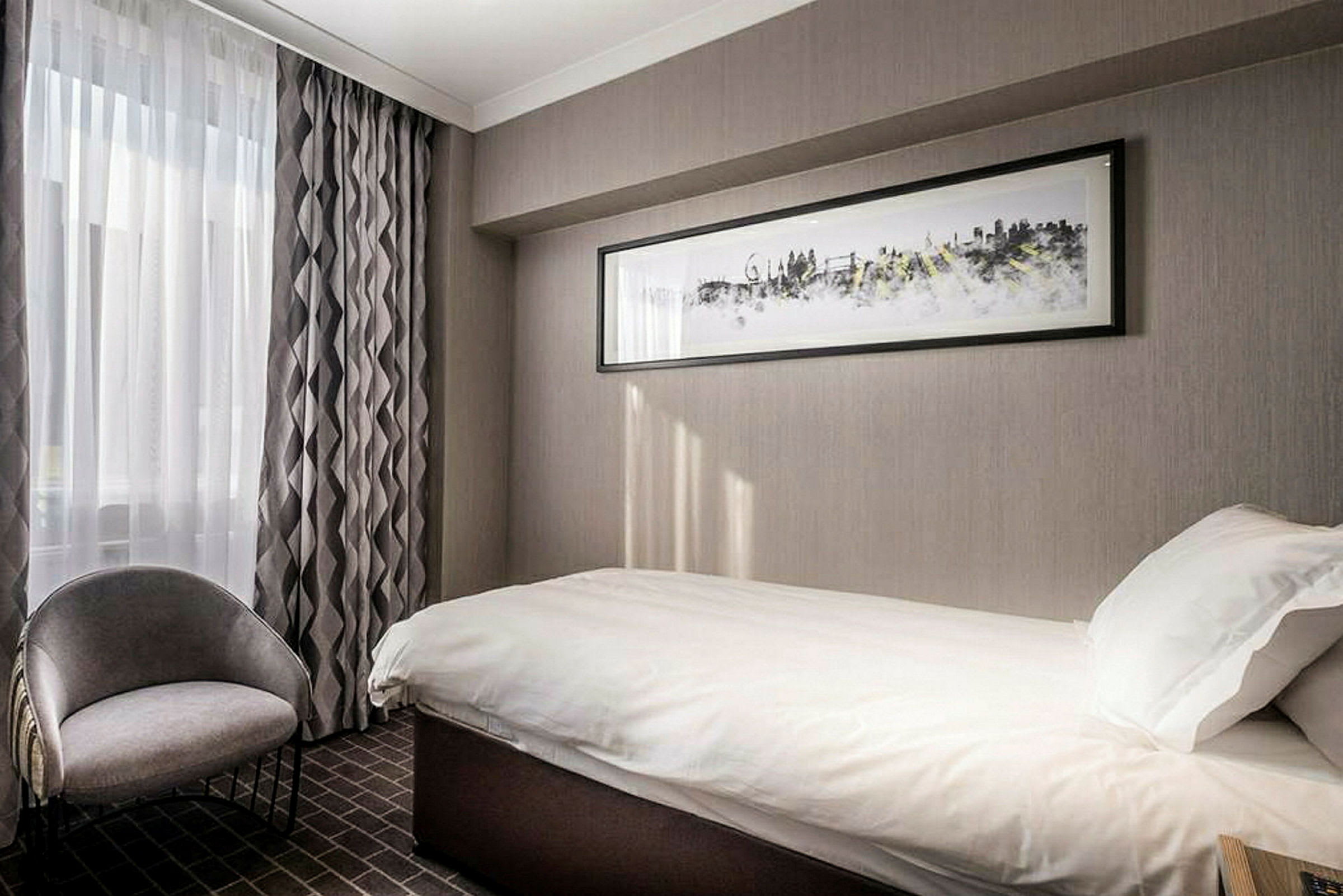 Hotelværelse med enkeltseng og stol, dekoreret i grå nuancer. (AI-genereret tekst)