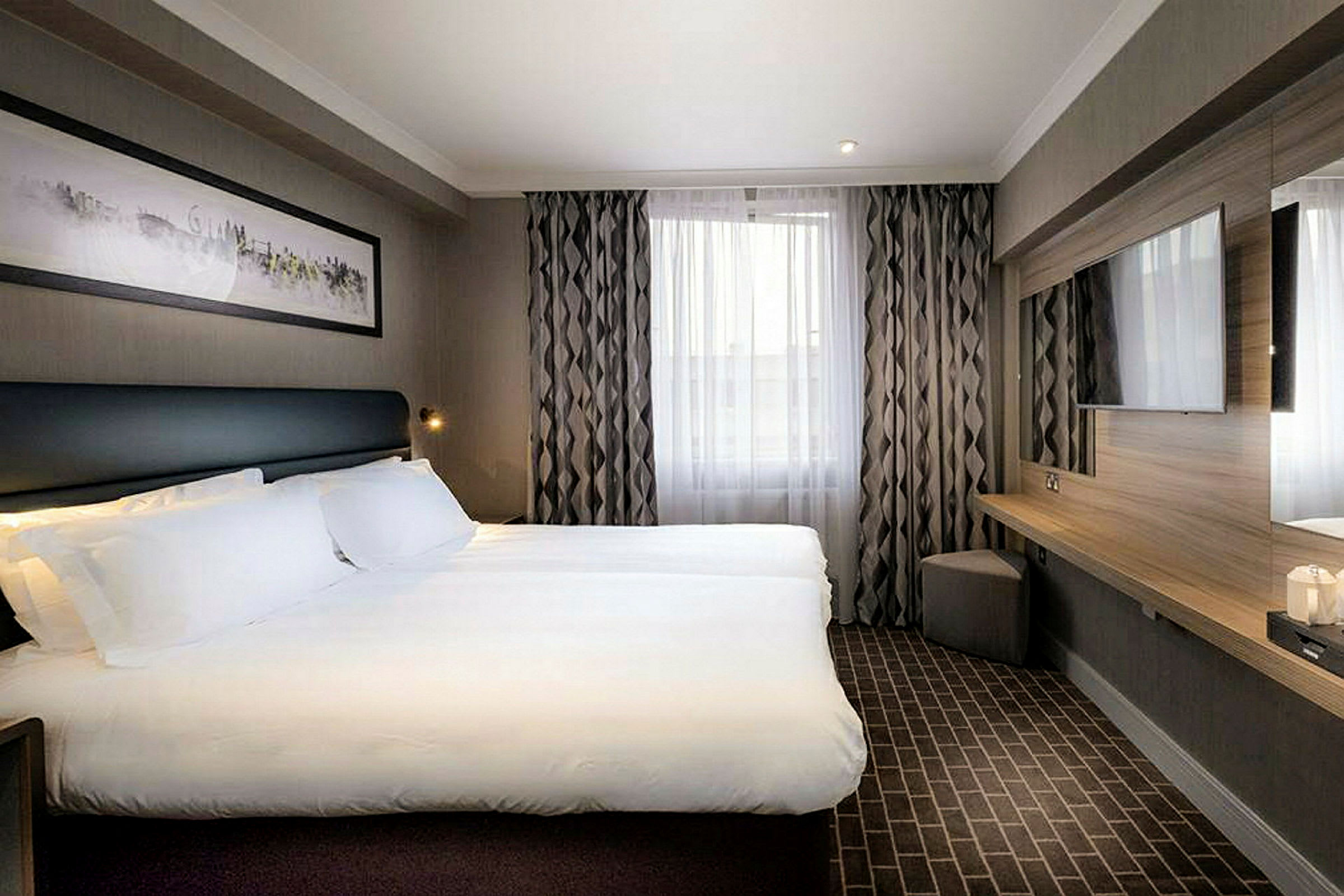 Moderne hotelværelse med en dobbeltseng, vægmonteret TV og vindue med gardiner. (AI-genereret tekst)