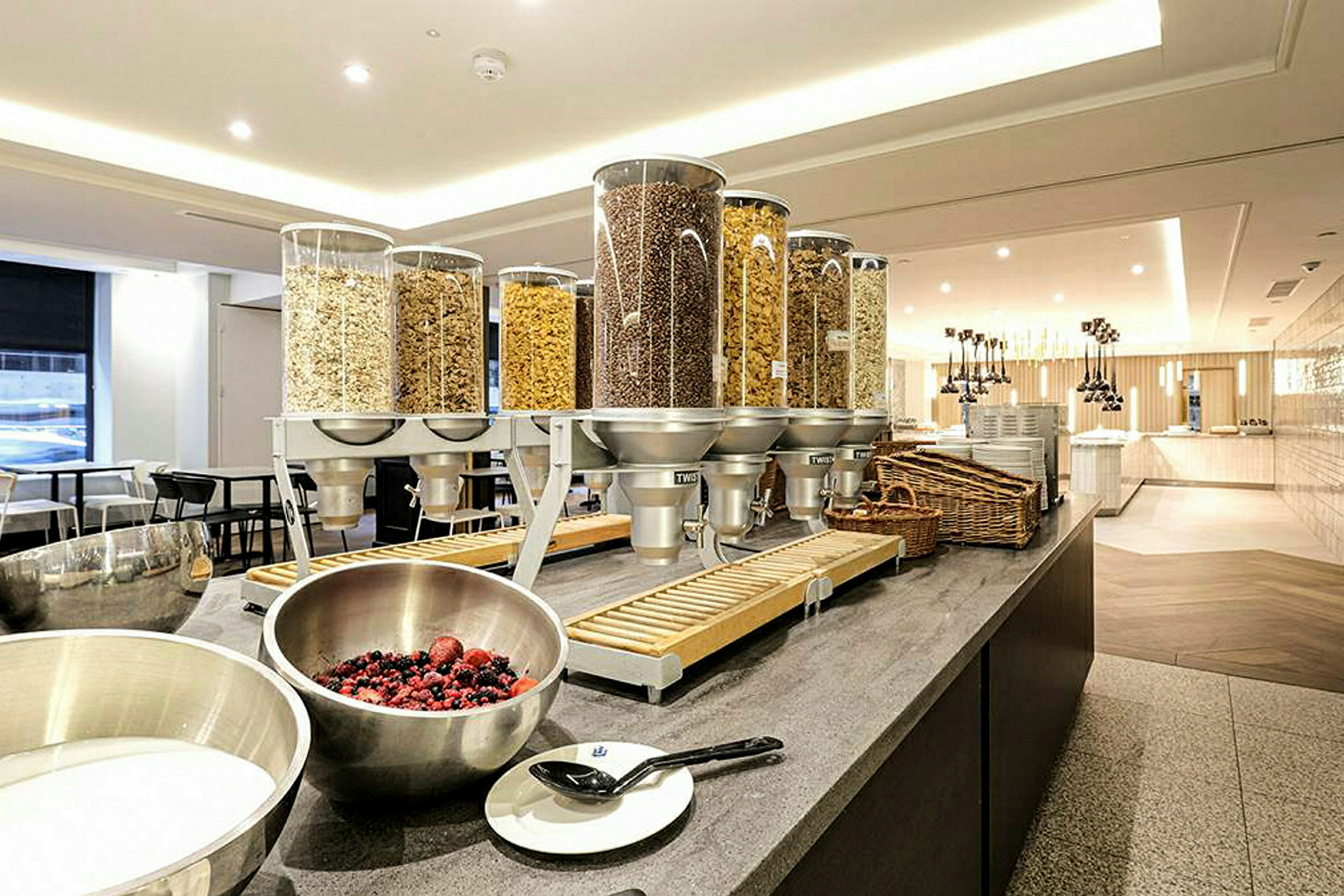 Billede af en morgenbuffet med korn i dispensere og skåle med mælk og bær. (AI-genereret tekst)