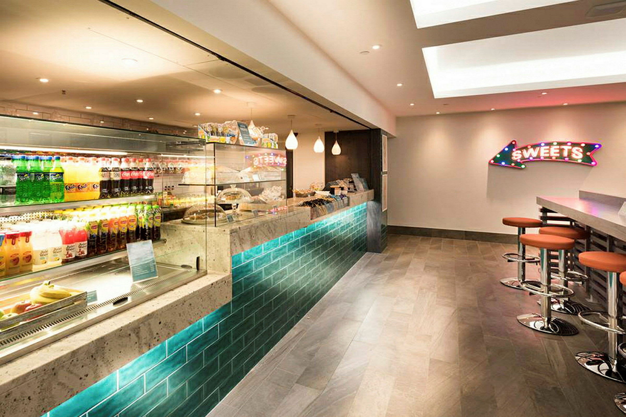 Billede af en moderne caféinteriør med en glasvitrine fyldt med drikkevarer og snacks samt siddepladser ved en bardisk. (AI-genereret tekst)