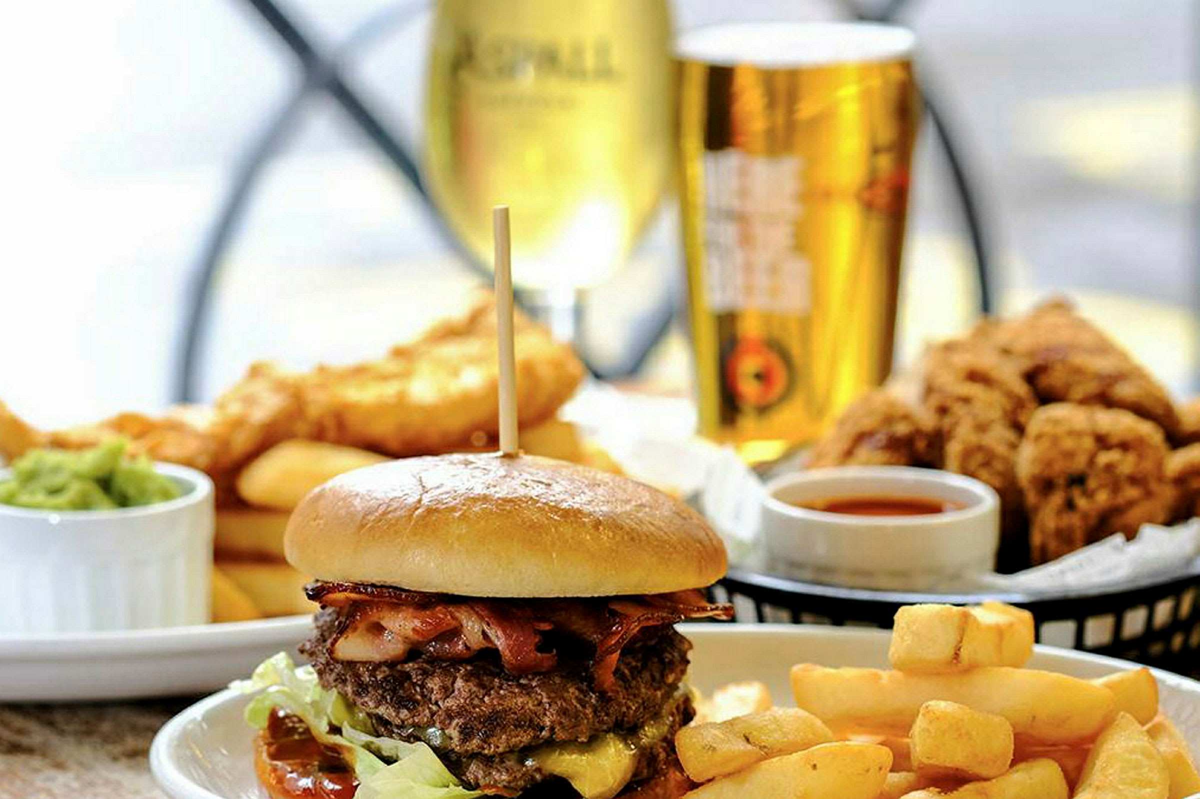 En oksekødburgere med pommes frites og tilbehør, drikke og frituremad i baggrunden. (AI-genereret tekst)