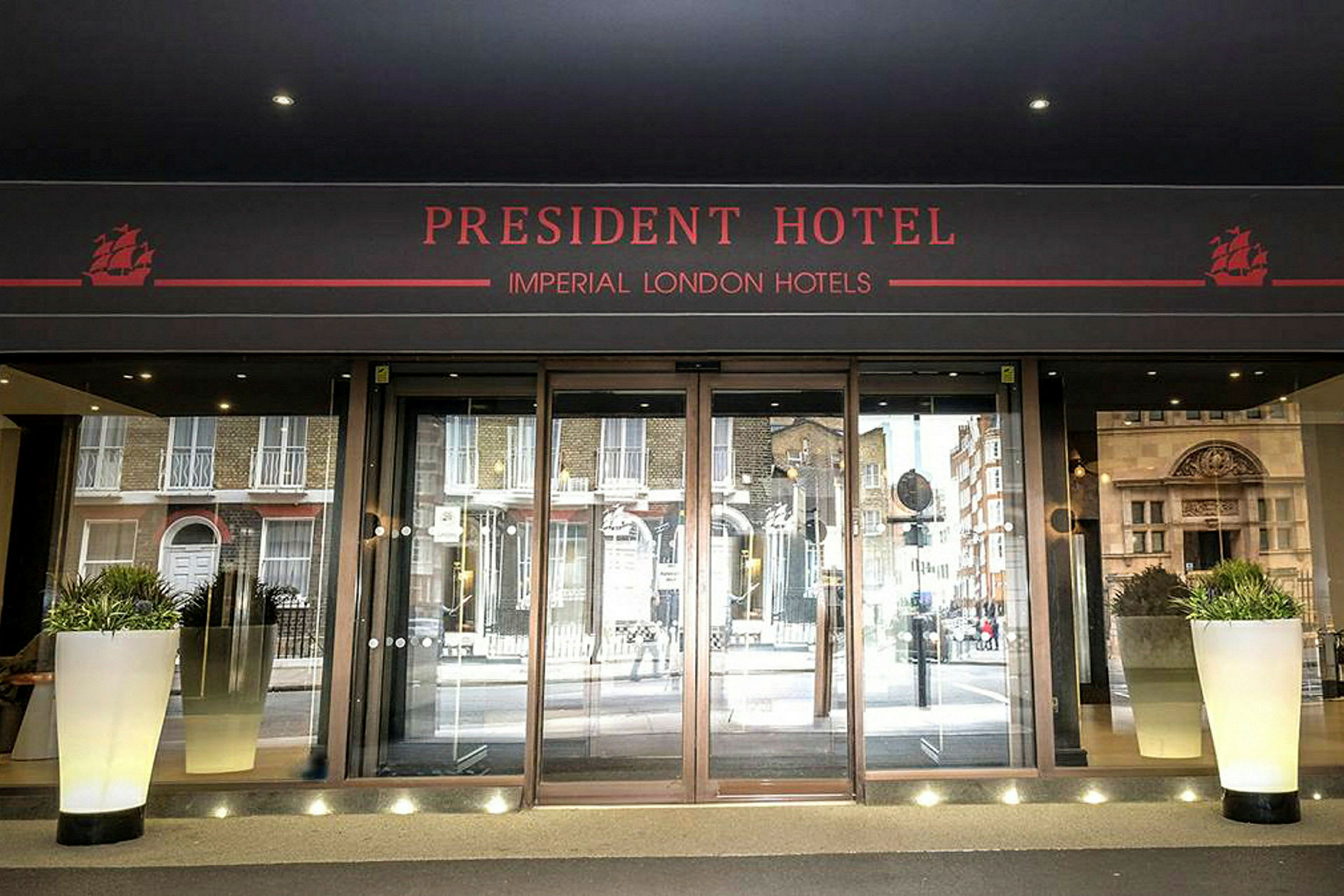 Hovedindgangen til President Hotel med glasdøre og blomsterkrukker. (AI-genereret tekst)