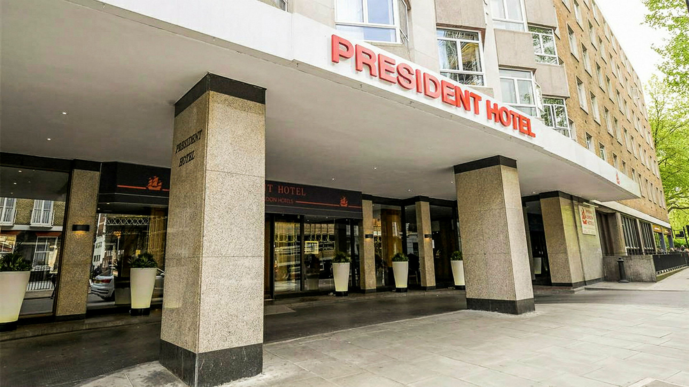 Forsiden af President Hotel med indgang og skilt. (AI-genereret tekst)