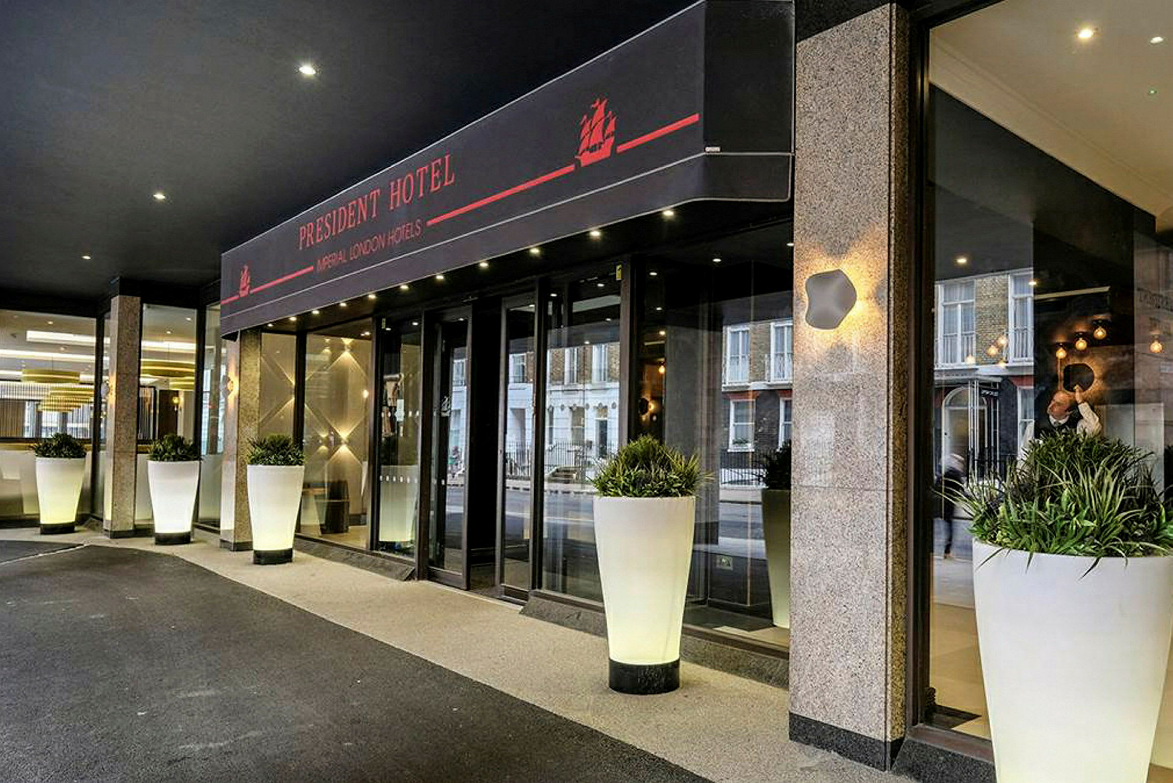 Indgangen til President Hotel, med store hvide blomsterkrukker. (AI-genereret tekst)