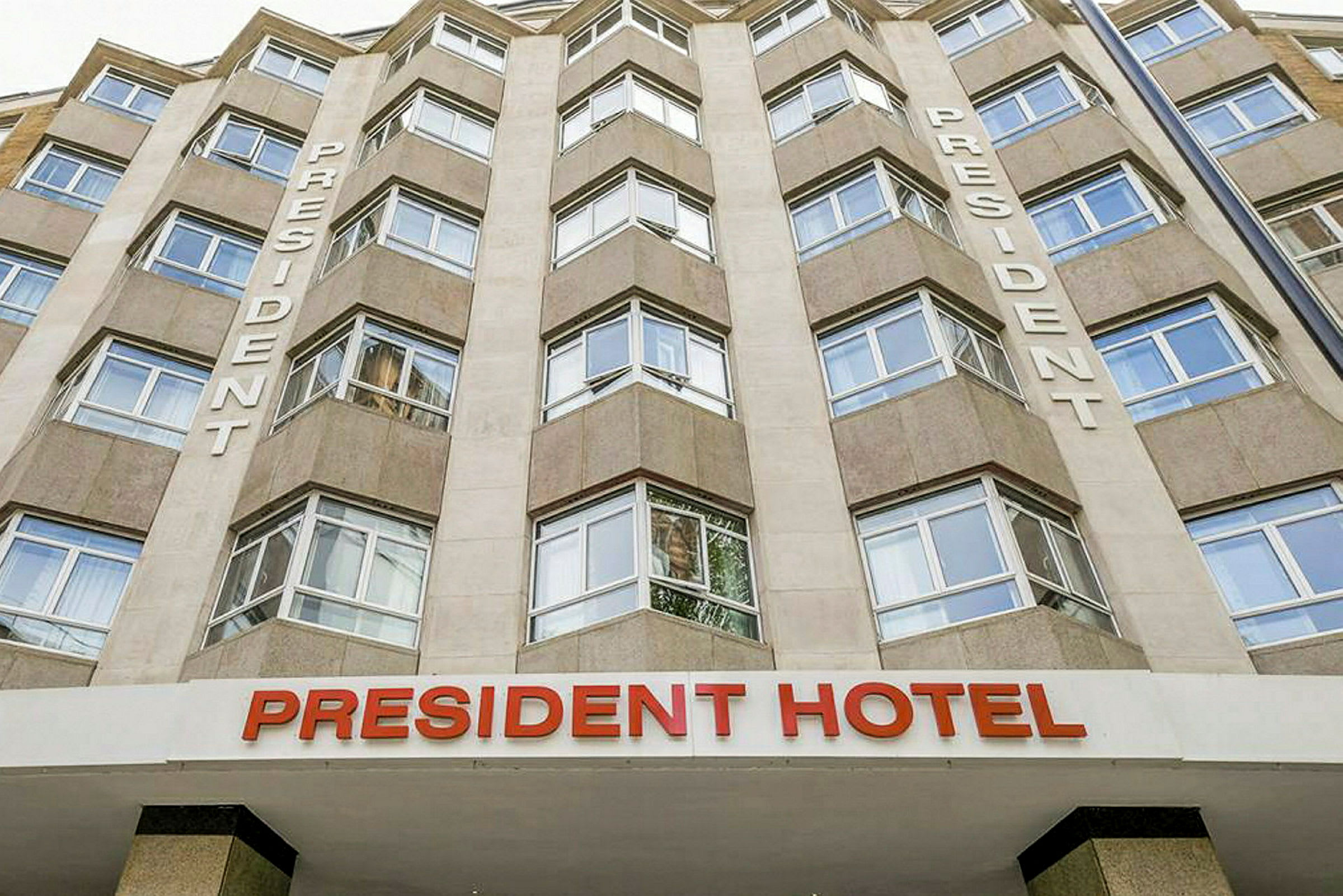 Klassisk facade af President Hotel med store vinduer og teksten 'President' på væggen. (AI-genereret tekst)