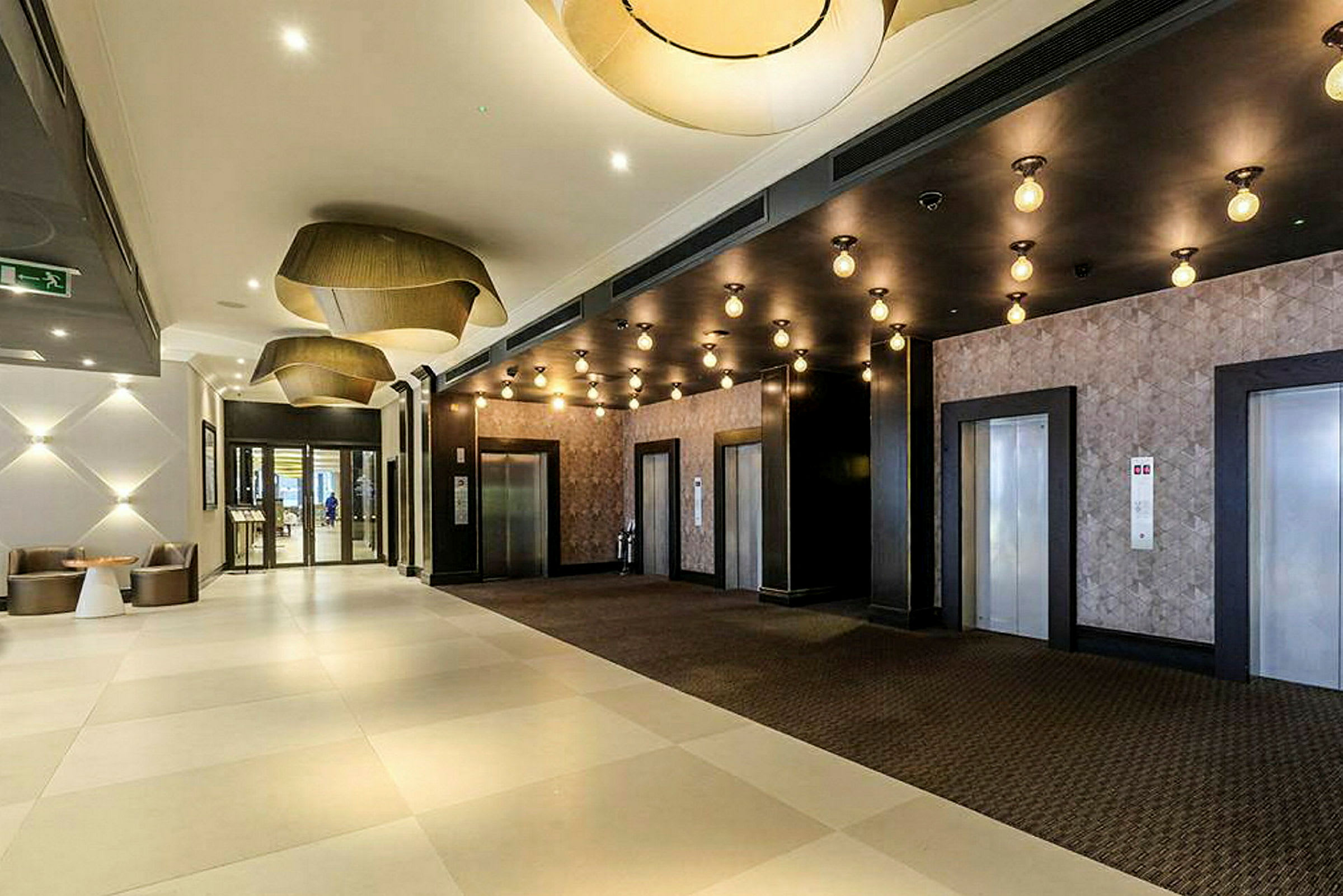 Hotellobby med tre elevatorer og moderne lamper. (AI-genereret tekst)
