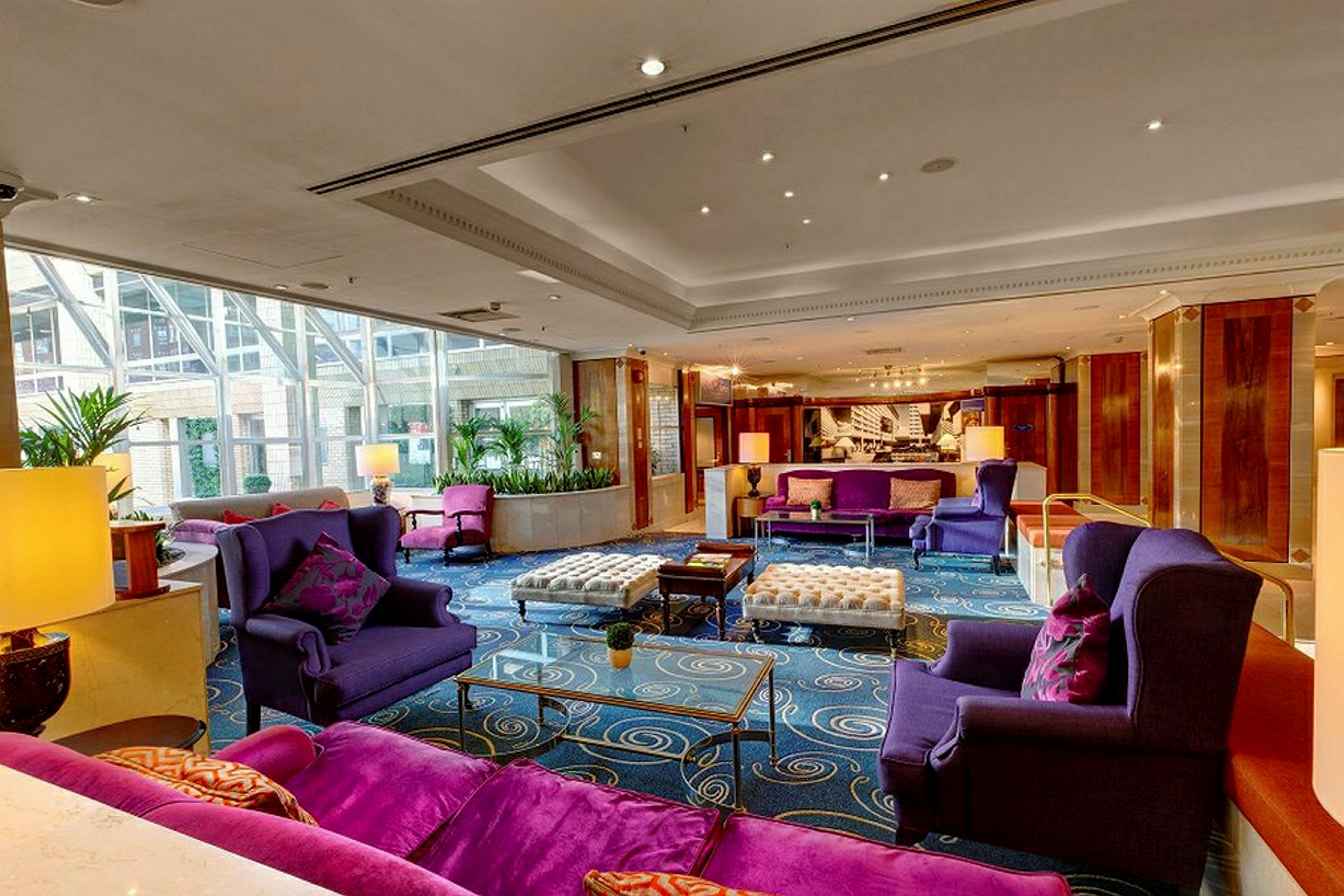 En hotellobby med lilla lænestole og sofaer samt glasborde og dekorative elementer. (AI-genereret tekst)