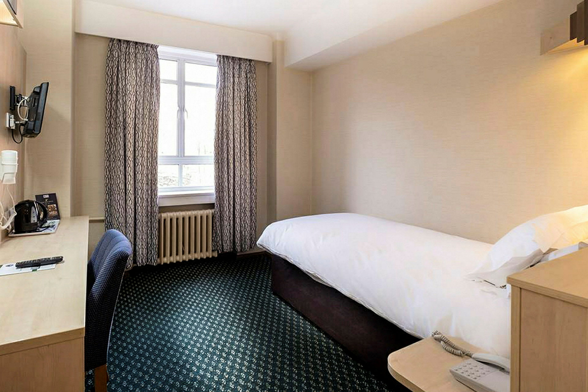 Et hotelværelse med en enkeltseng og skrivebord ved vinduet. (AI-genereret tekst)
