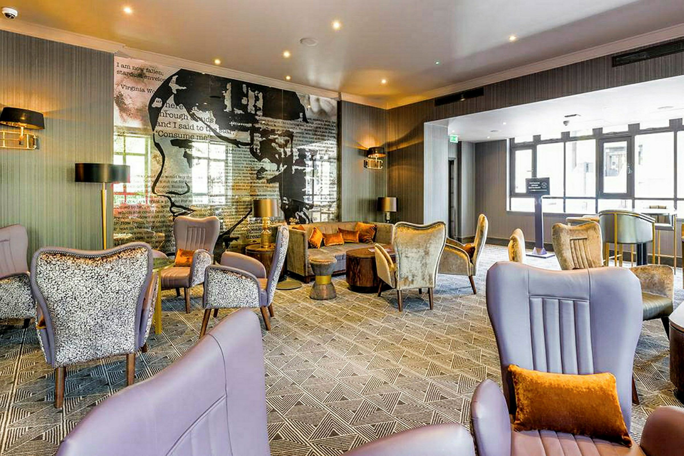 Et moderne hotelrum med komfortable siddemøbler, elegante dekorationer og en vægtapet med tekst og kunst. Store vinduer slipper naturligt lys ind. (AI-genereret tekst)