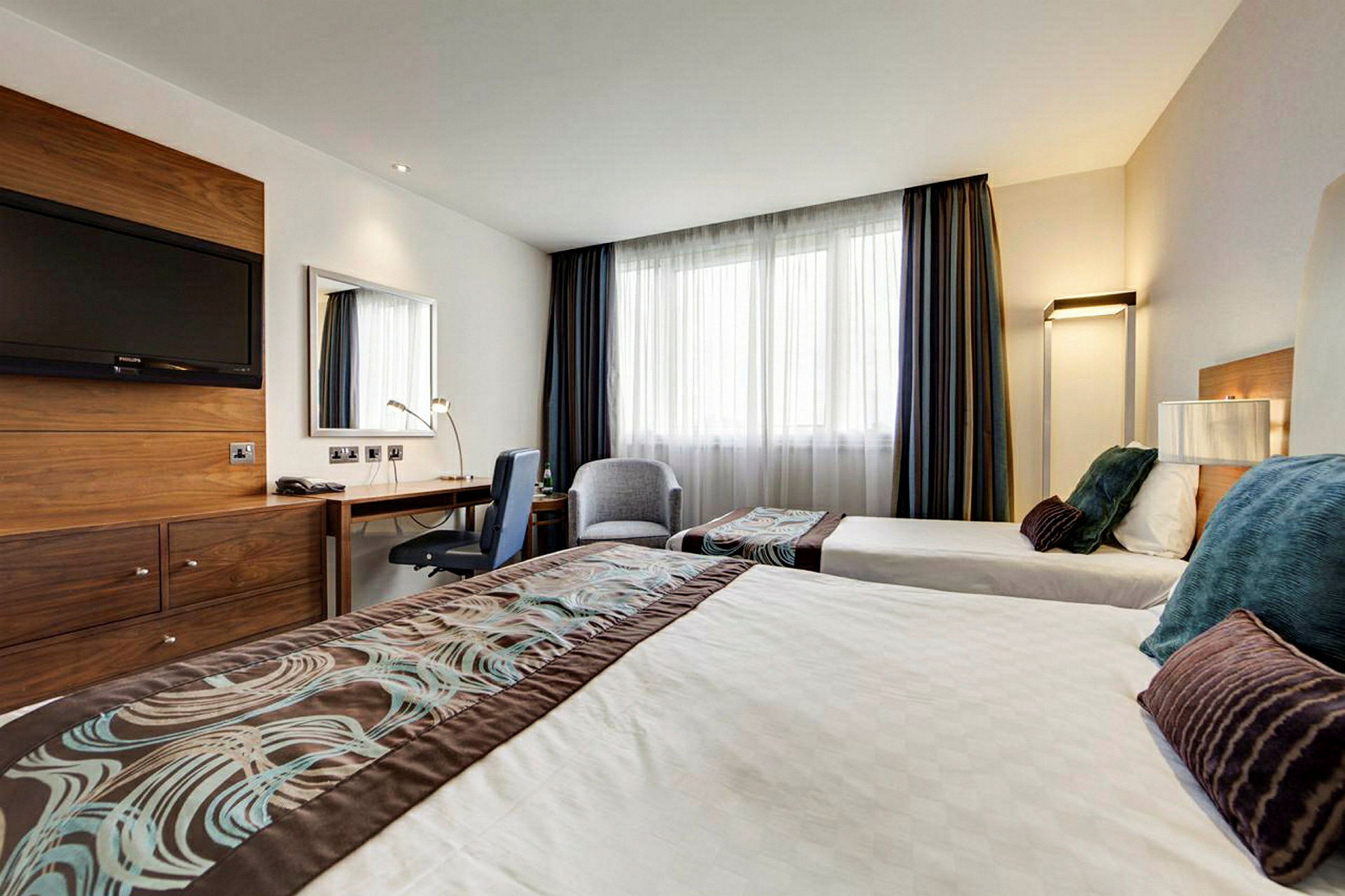Et hotelværelse med to enkeltsenge, et skrivebord og et tv på væggen. (AI-genereret tekst)