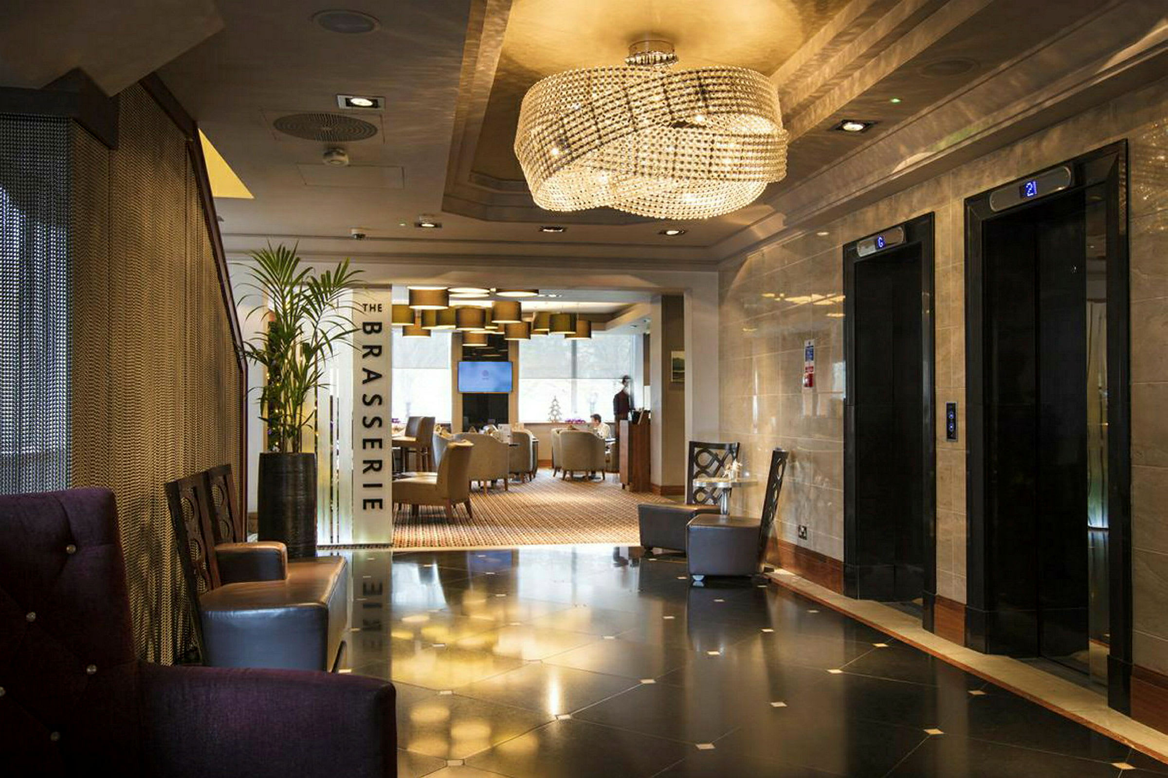 Hotellets lobby med elevatorer til højre og indgang til restauranten 'The Brasserie' lige frem. (AI-genereret tekst)