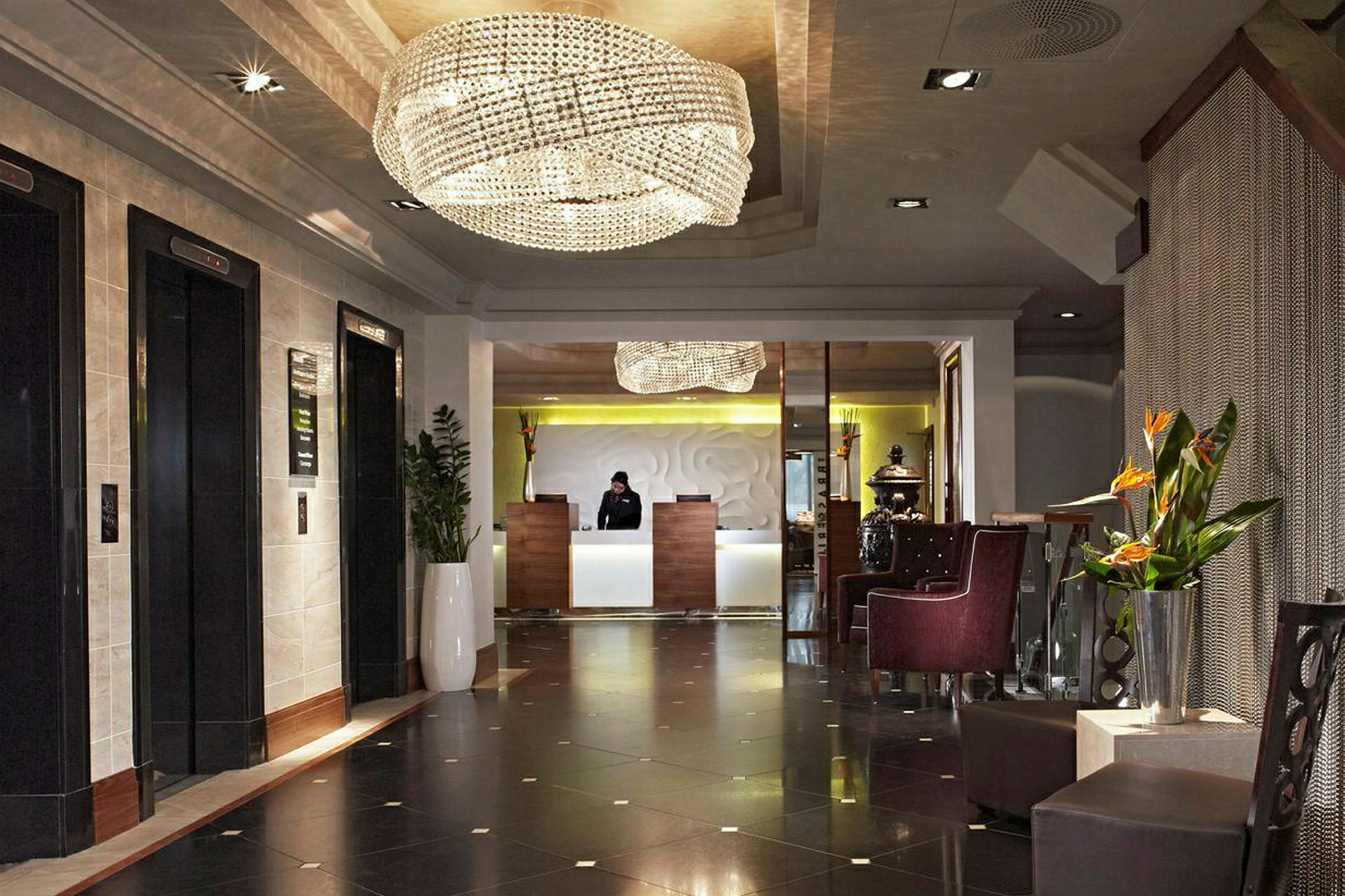 Hotellets foyer med reception og venteområde, dekoreret med lysekrone og planter. (AI-genereret tekst)