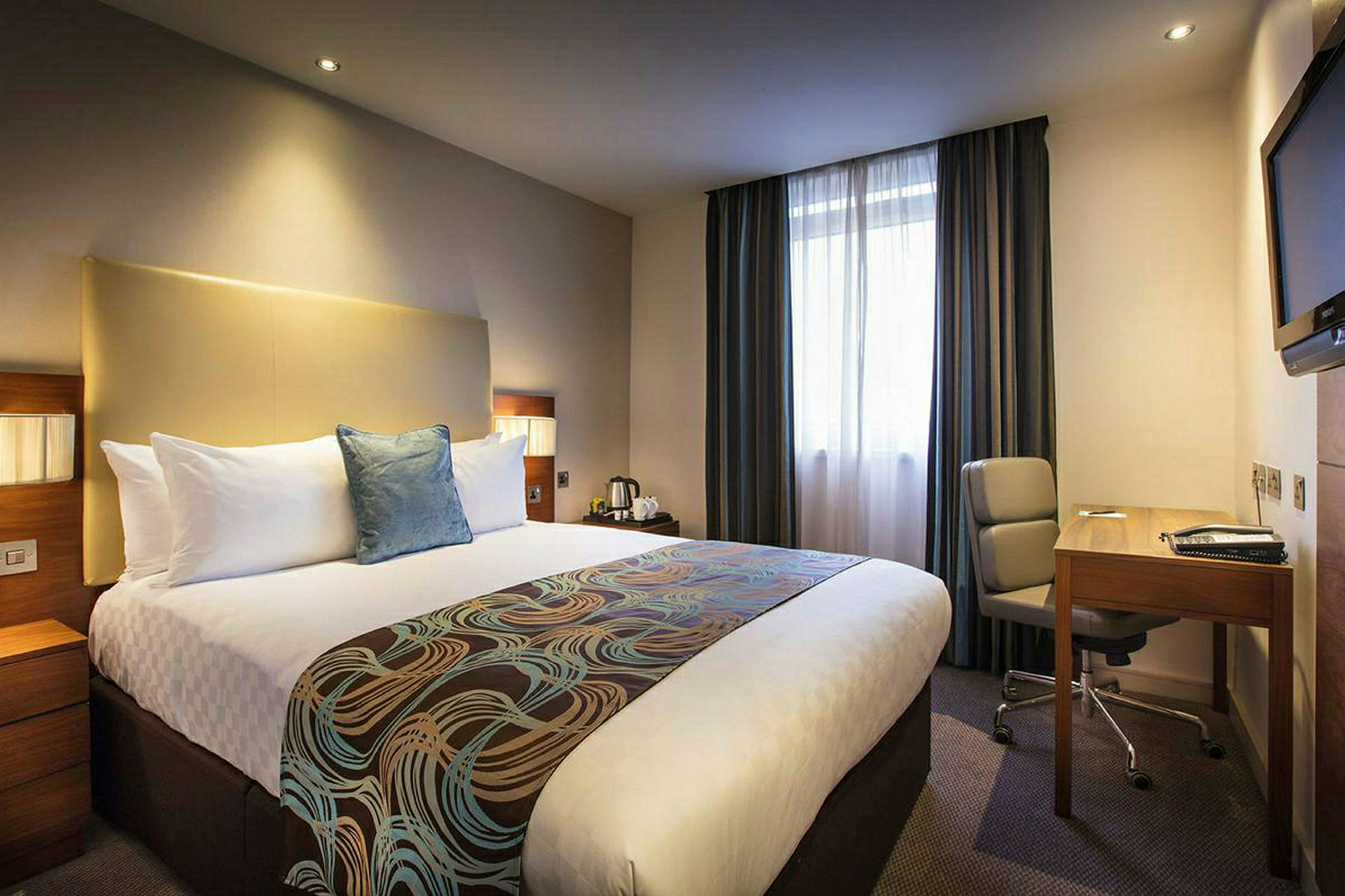 Hotelværelse med en stor seng, skrivebord og stol. (AI-genereret tekst)