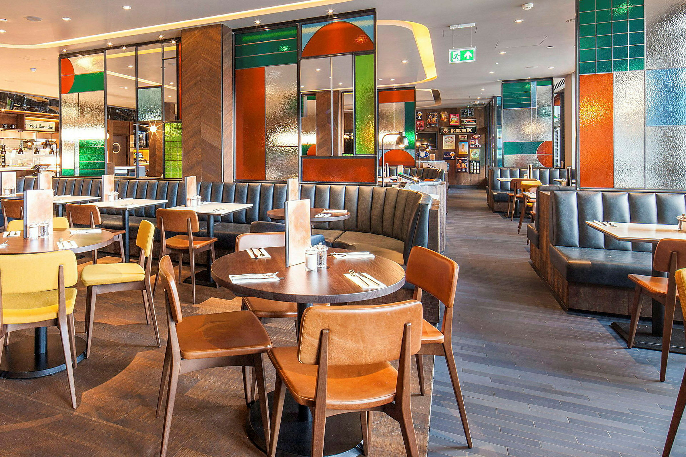 En restaurant med borde, stole og båse, indrettet med farvede glasdetaljer. (AI-genereret tekst)