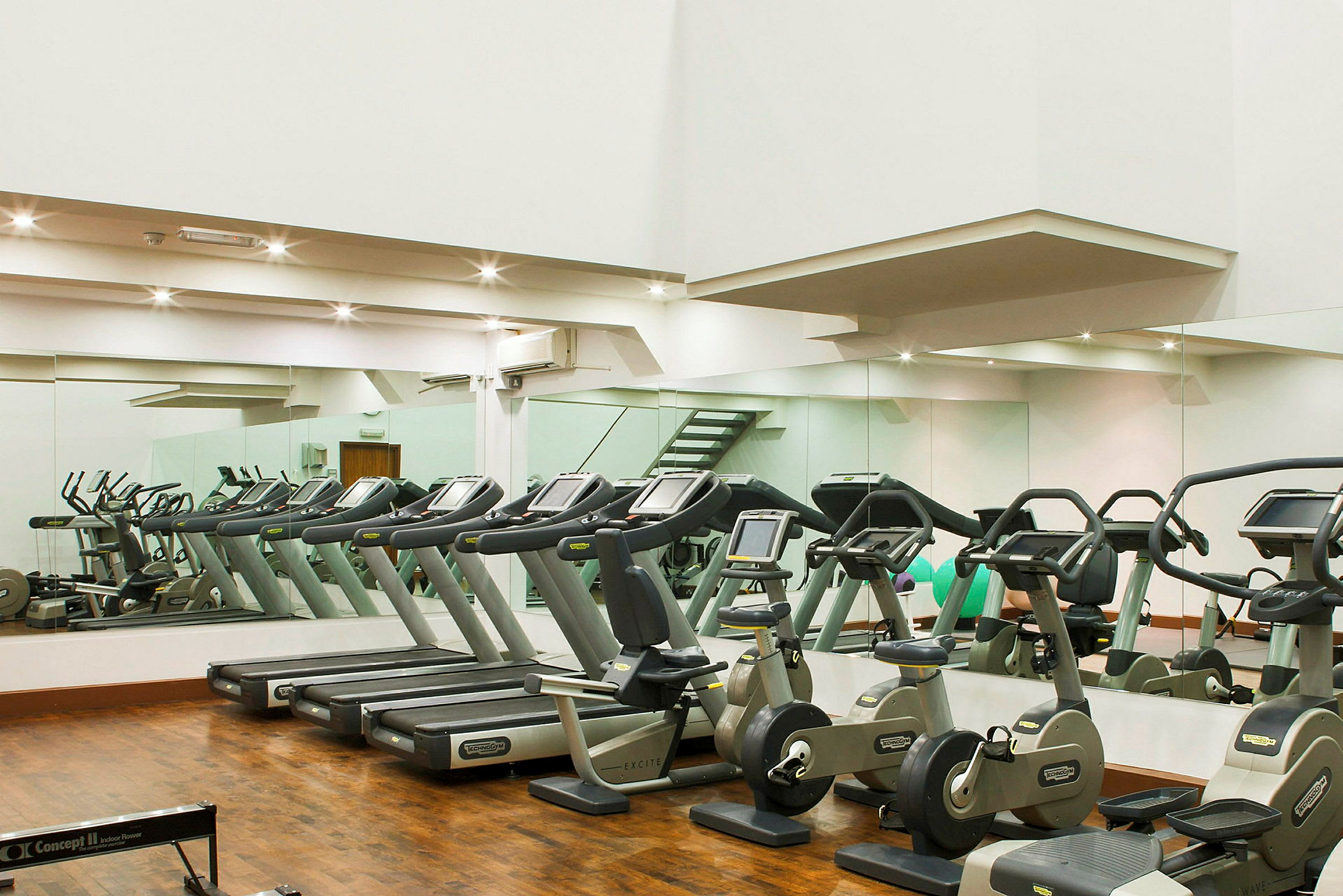 Et fitnesscenter med træningsmaskiner, herunder løbebånd og motionscykler foran spejle. (AI-genereret tekst)