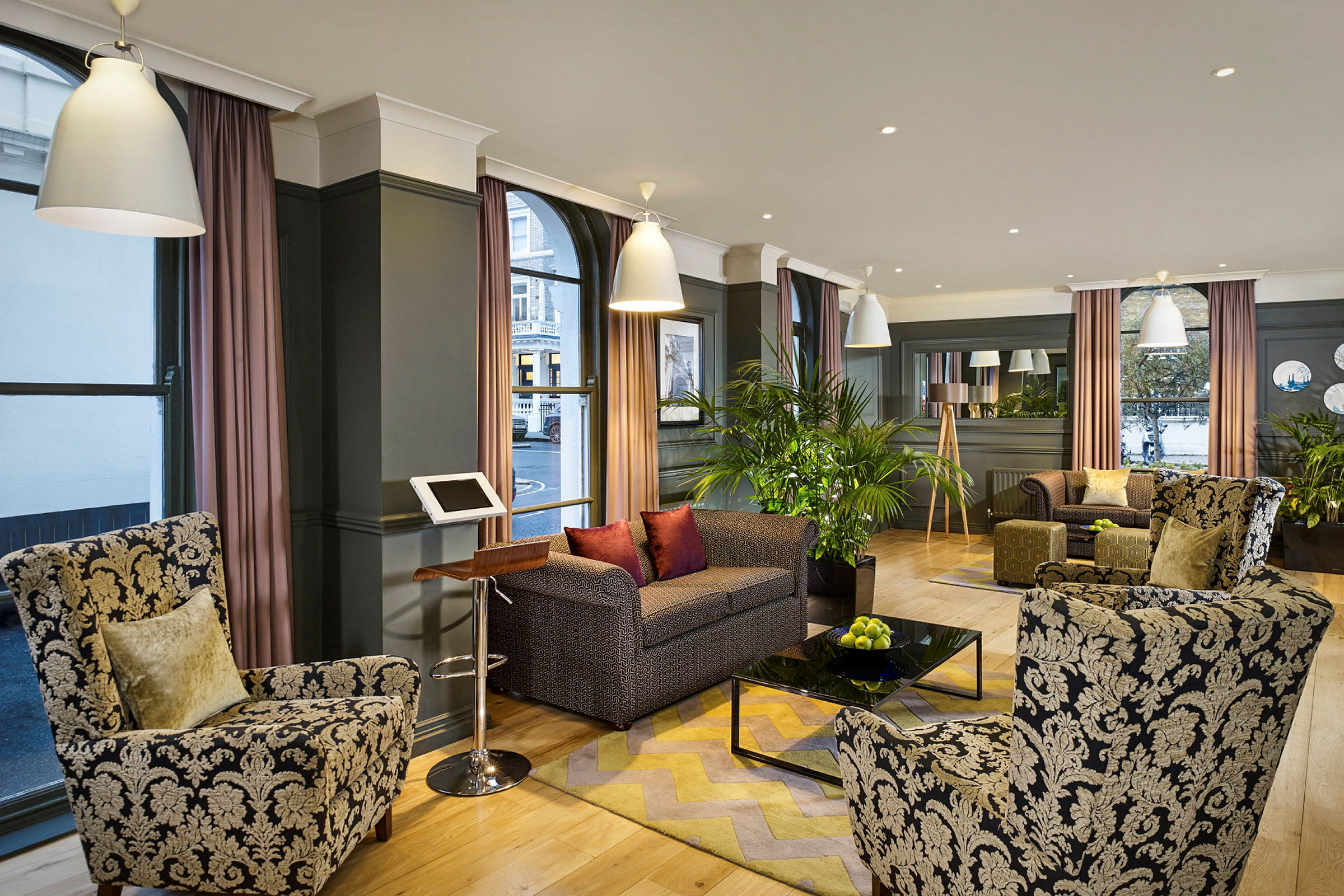 En hotellobby med lænestole og sofaer omkring et sofabord samt dekoration med planter. (AI-genereret tekst)