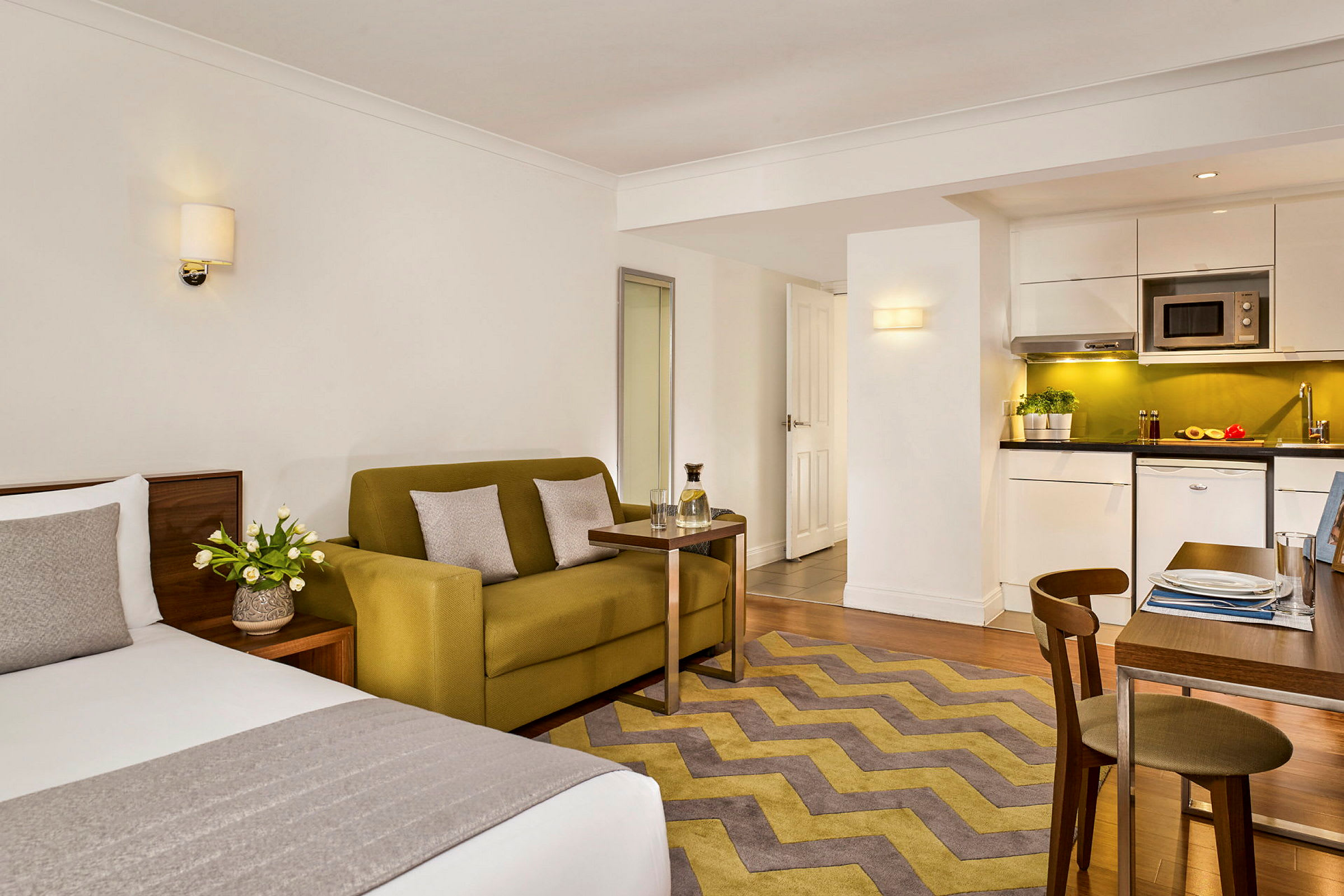 Et moderne hotelværelse med seng, sofa, bord og et køkken med spiseområde. (AI-genereret tekst)