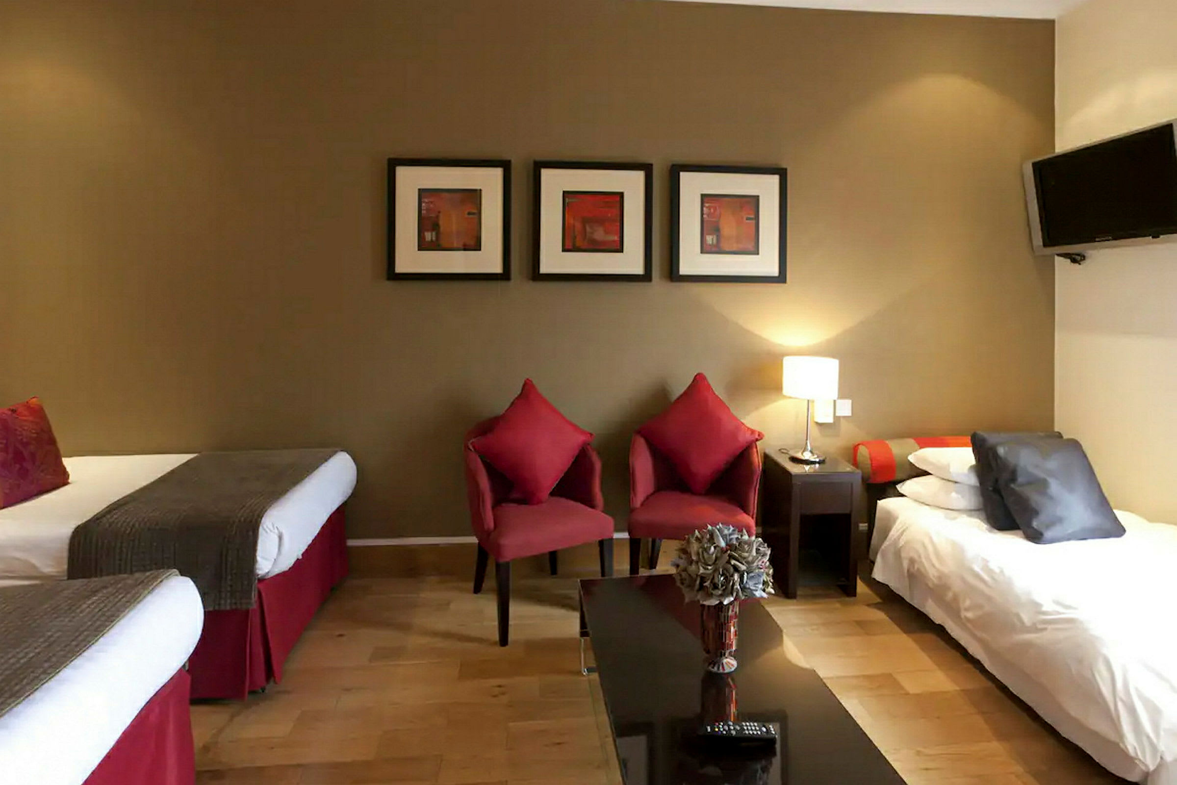 Hotelværelse med to enkeltsenge, to røde stole og et bord med blomster. (AI-genereret tekst)