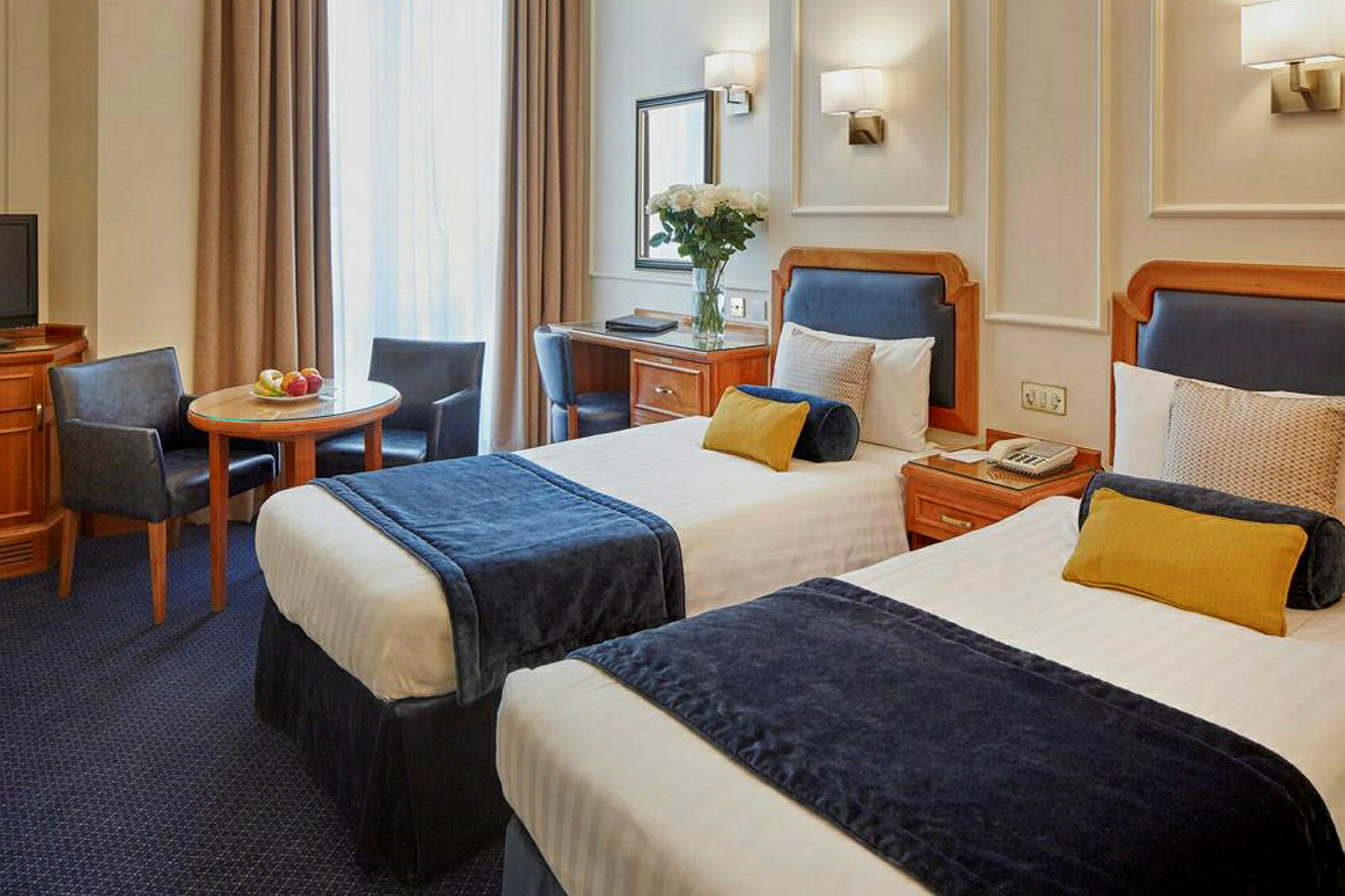 Hotelværelse med to enkeltsenge, bord og stole. (AI-genereret tekst)