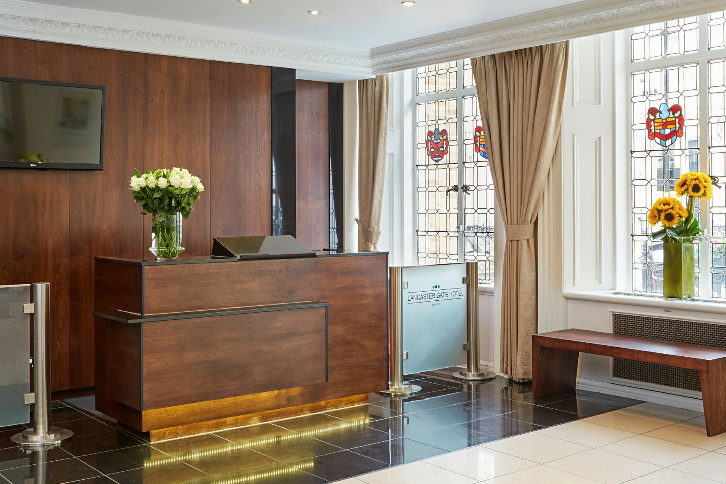Hotelreception med et skranke af træ og en vase med hvide blomster, ved siden af vinduer med farvede dekorationer. (AI-genereret tekst)