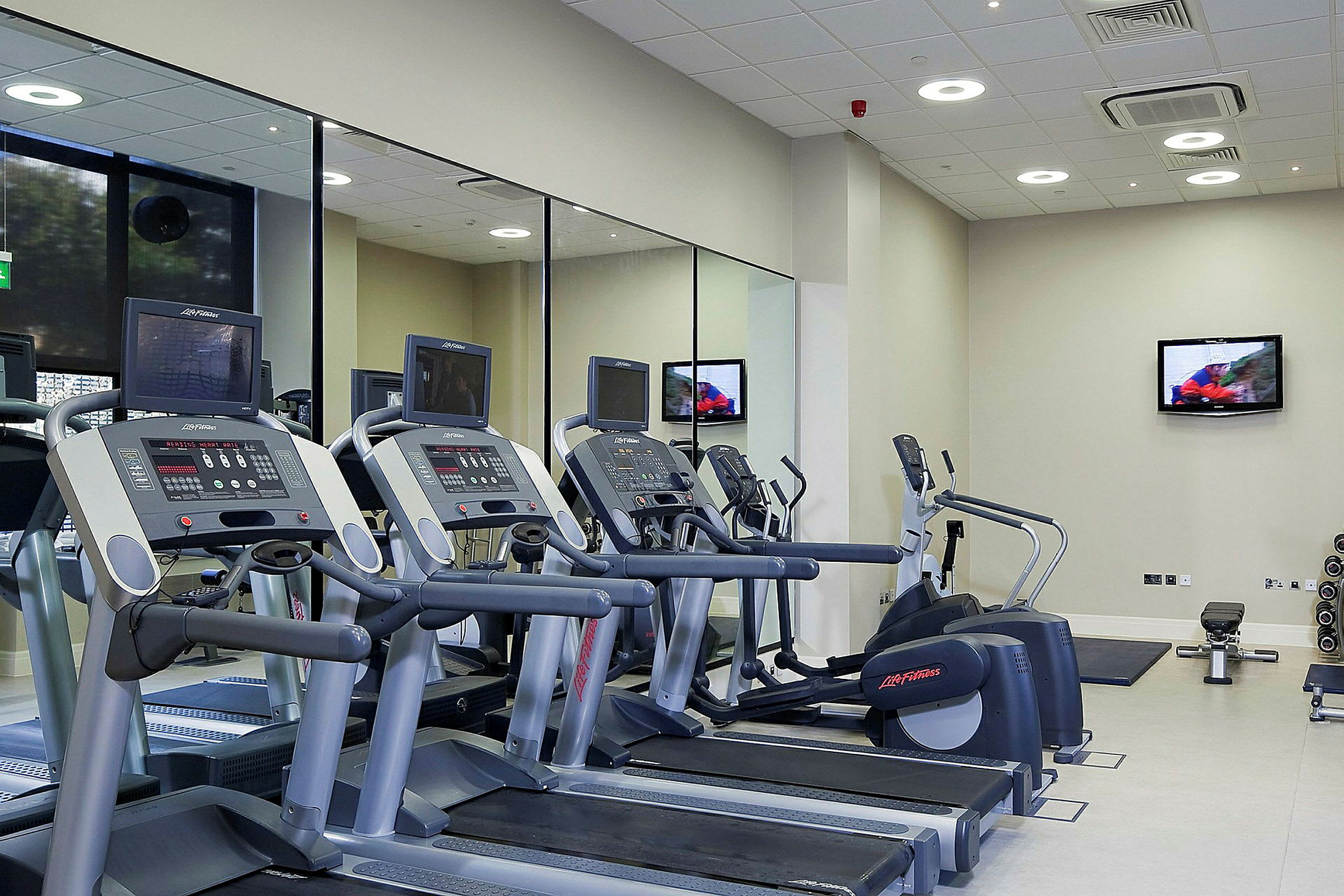 Fitnessrum med træningsmaskiner og spejlvæg. (AI-genereret tekst)