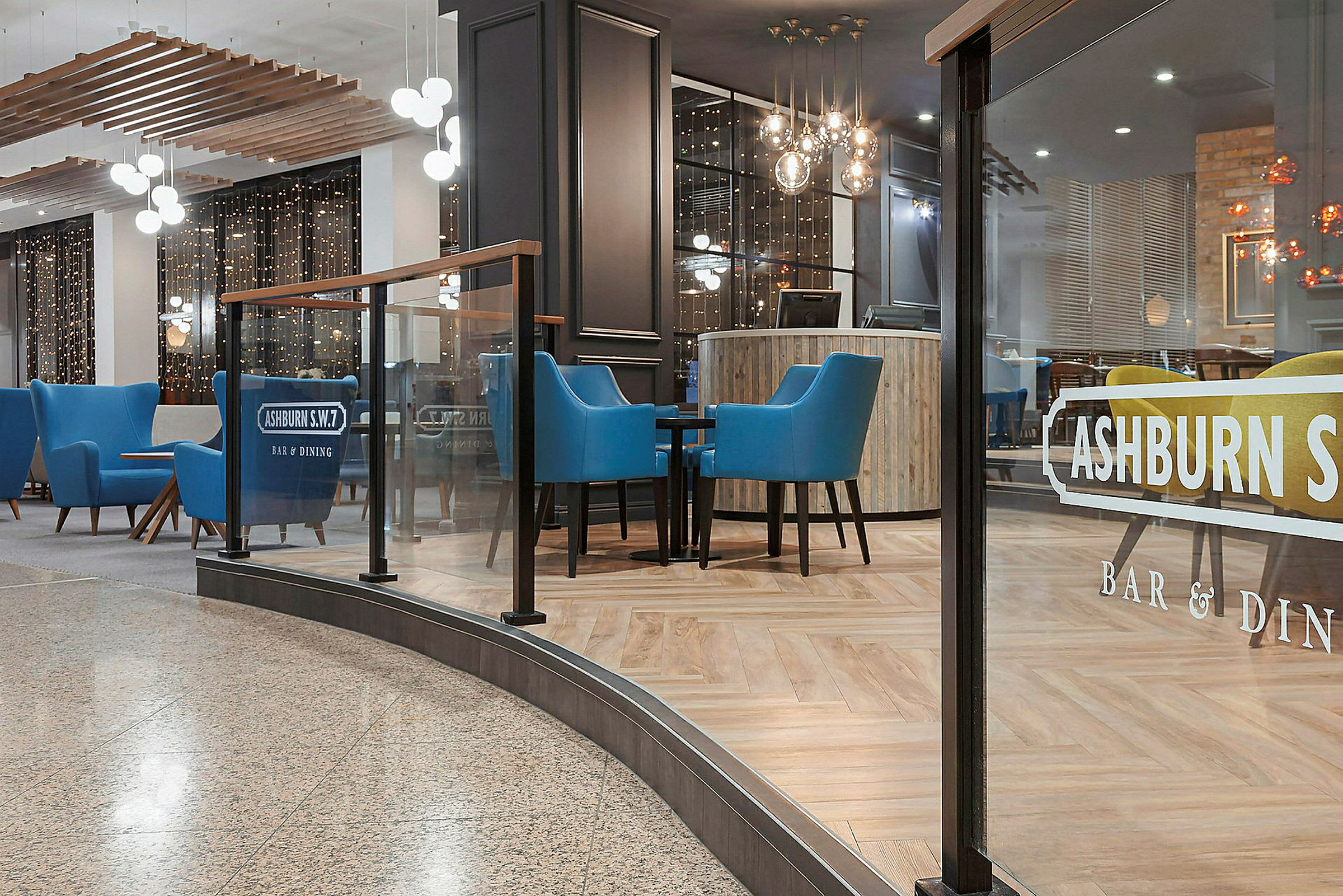 Interiør af en elegant restaurant med blå lænestole og glasvæg. (AI-genereret tekst)