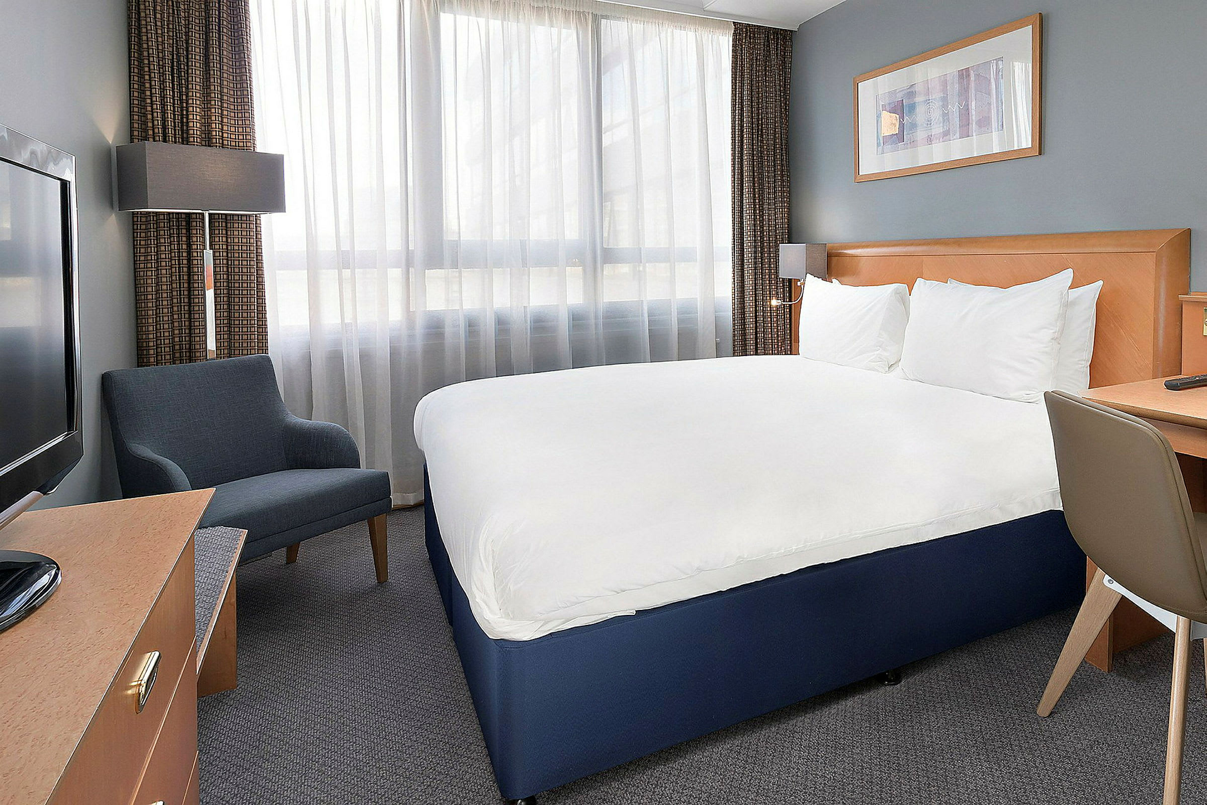 Hotelværelse med en dobbeltseng, lænestol, skrivebord og tv. (AI-genereret tekst)