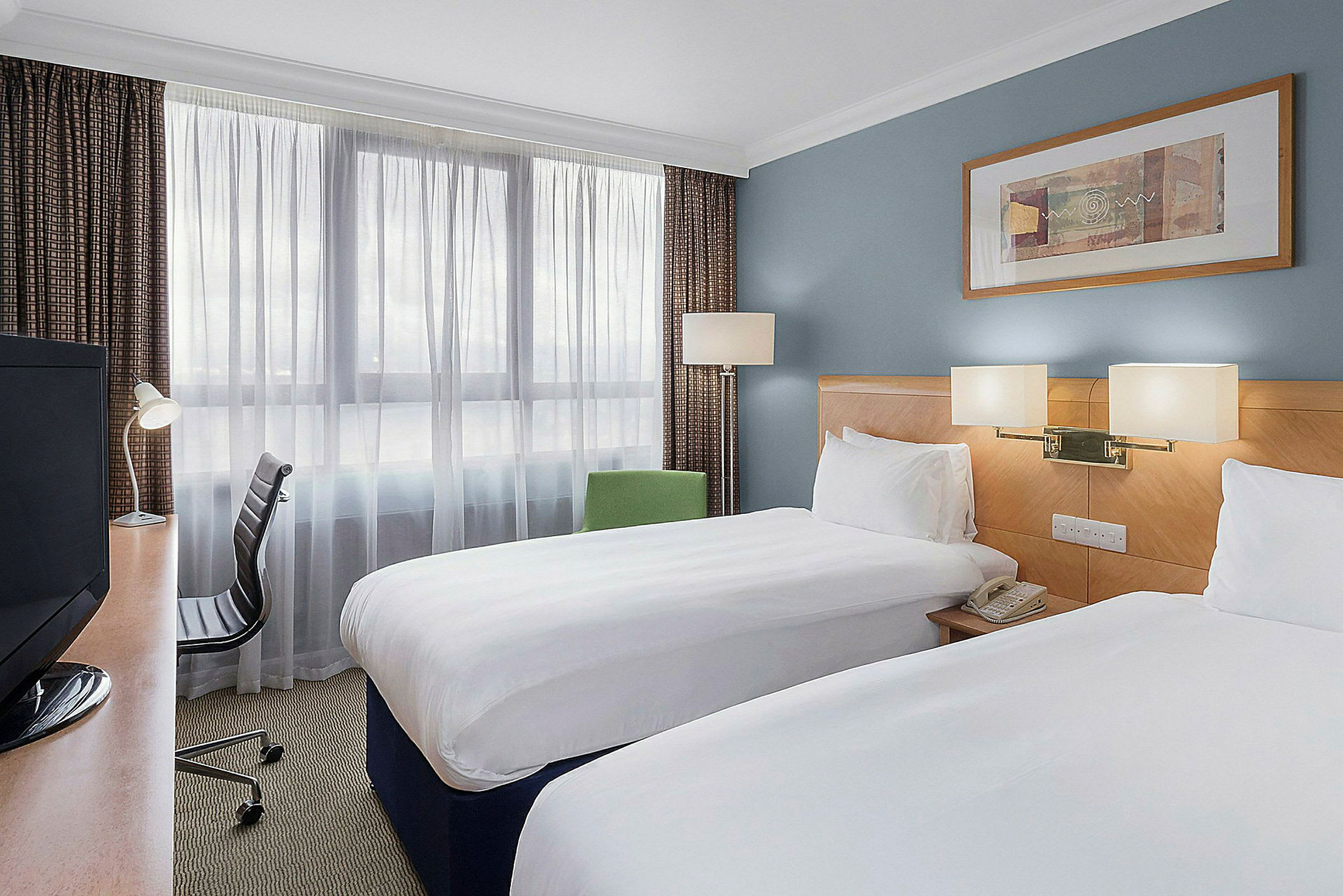 Hotelværelse med to enkeltsenge, skrivebord og stol. (AI-genereret tekst)