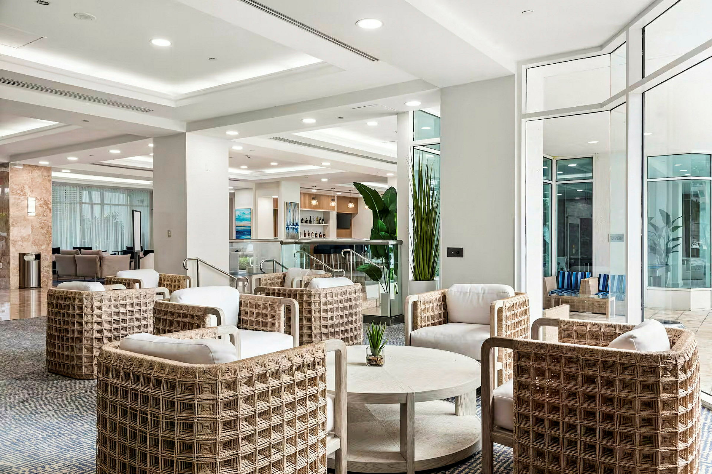 En moderne hotellobby med siddegrupper i lyse farver og store vinduer. (AI-genereret tekst)