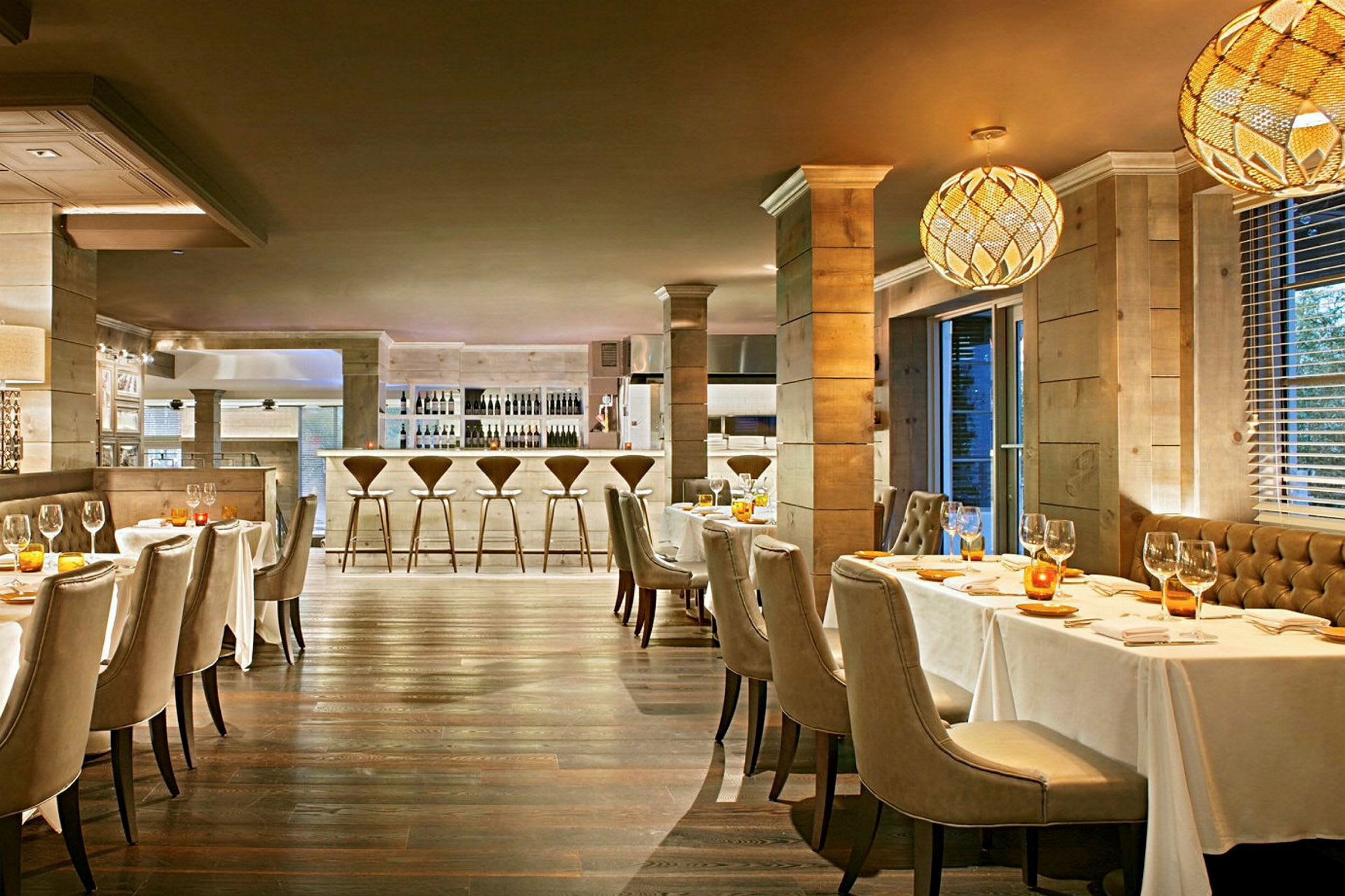 En elegant restaurant med borde dækket med hvide duge, polstrede stole og en bardisk i baggrunden. (AI-genereret tekst)