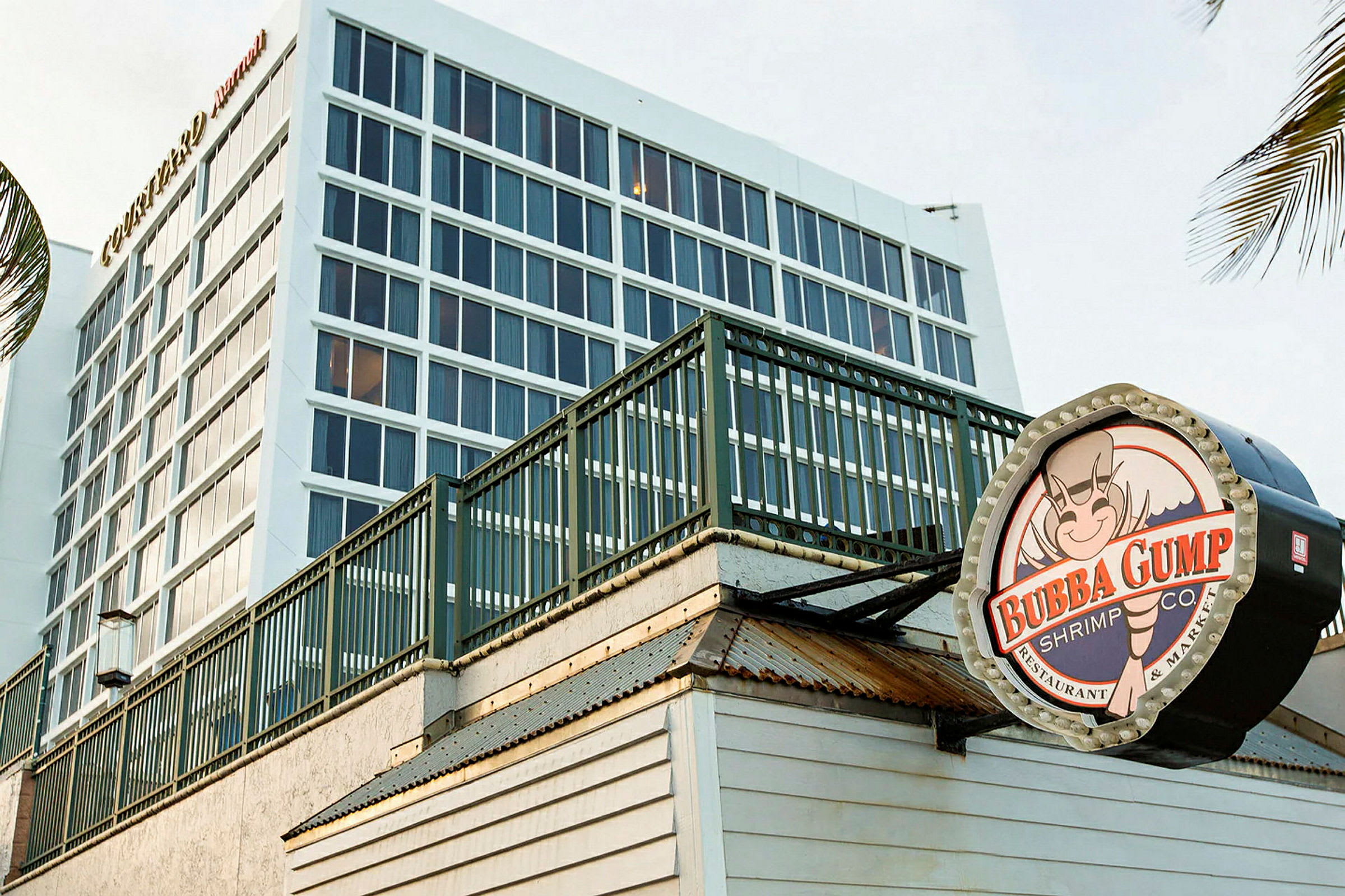 En moderne bygning i baggrunden med store vinduer, og i forgrunden et skilt for restauranten Bubba Gump Shrimp Co. (AI-genereret tekst)
