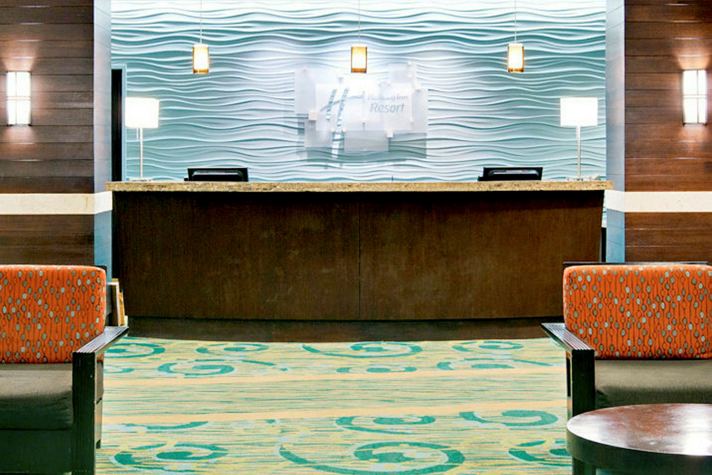 Hotelreception med en trædisk og marmorbordplade, baggrund med moderne bølgeformet design. Foran er der siddepladser med farverigt stofbetræk. (AI-genereret tekst)