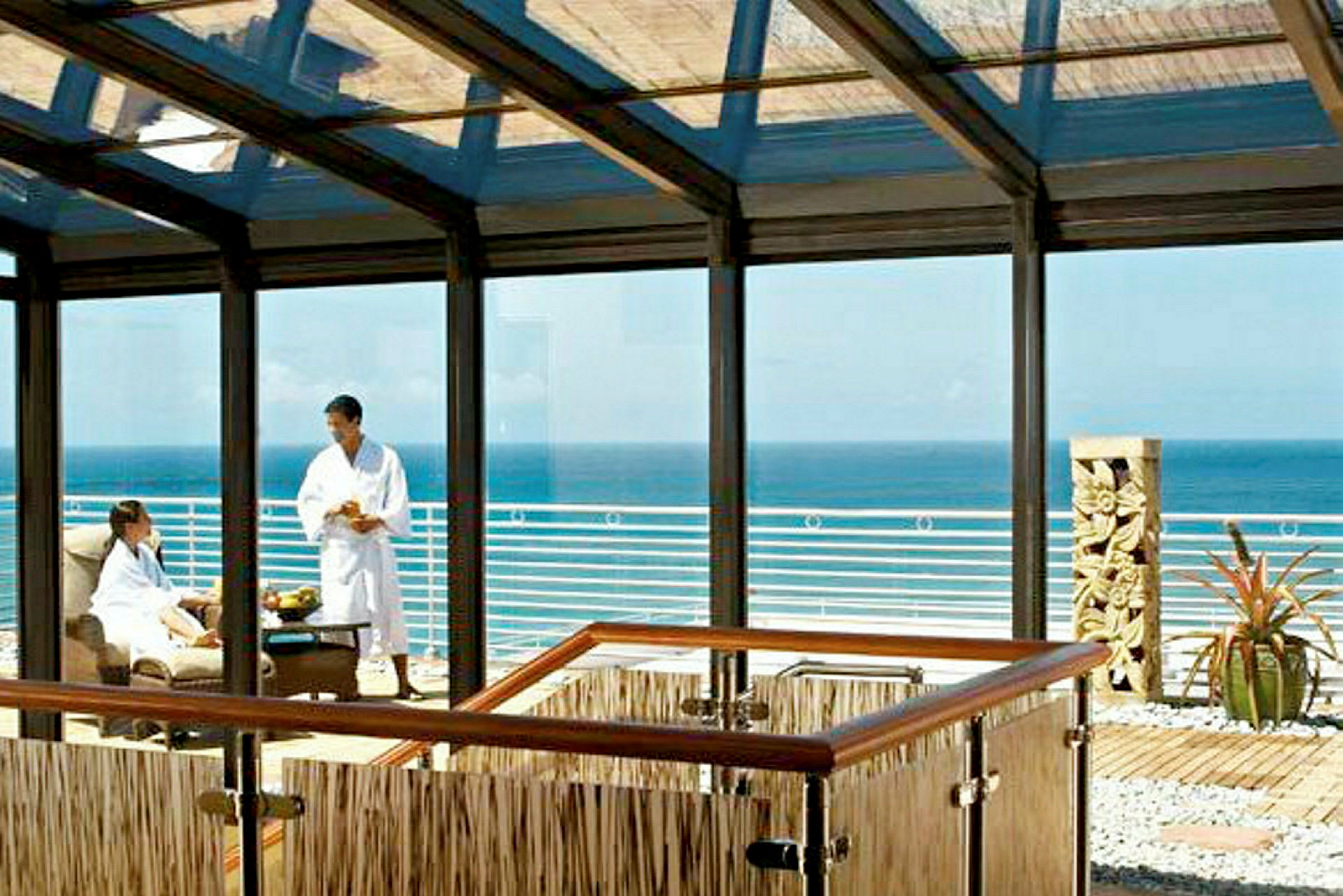 En indglaset lounge med udsigt over havet og en terrasse med en skulptur og planter. (AI-genereret tekst)
