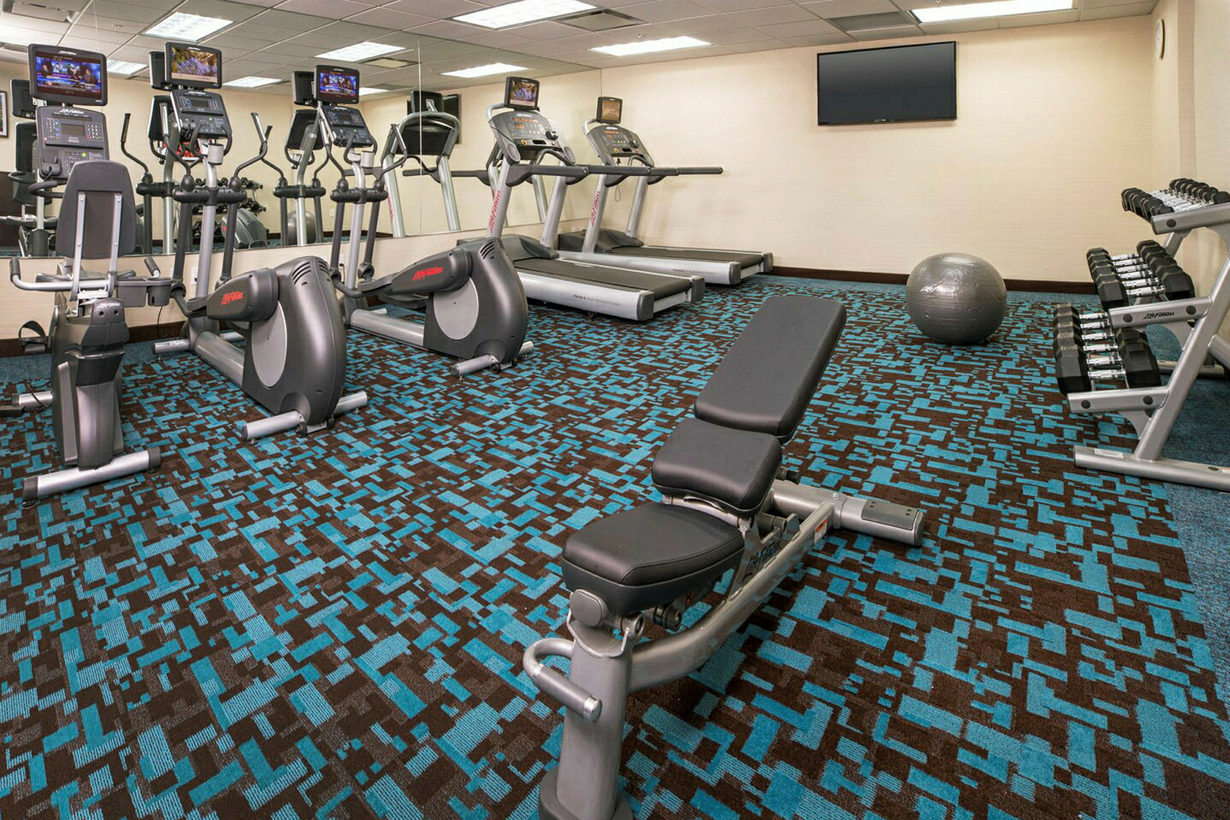 Fitnesscenter med træningsmaskiner, vægte, bænk og træningsbold. (AI-genereret tekst)