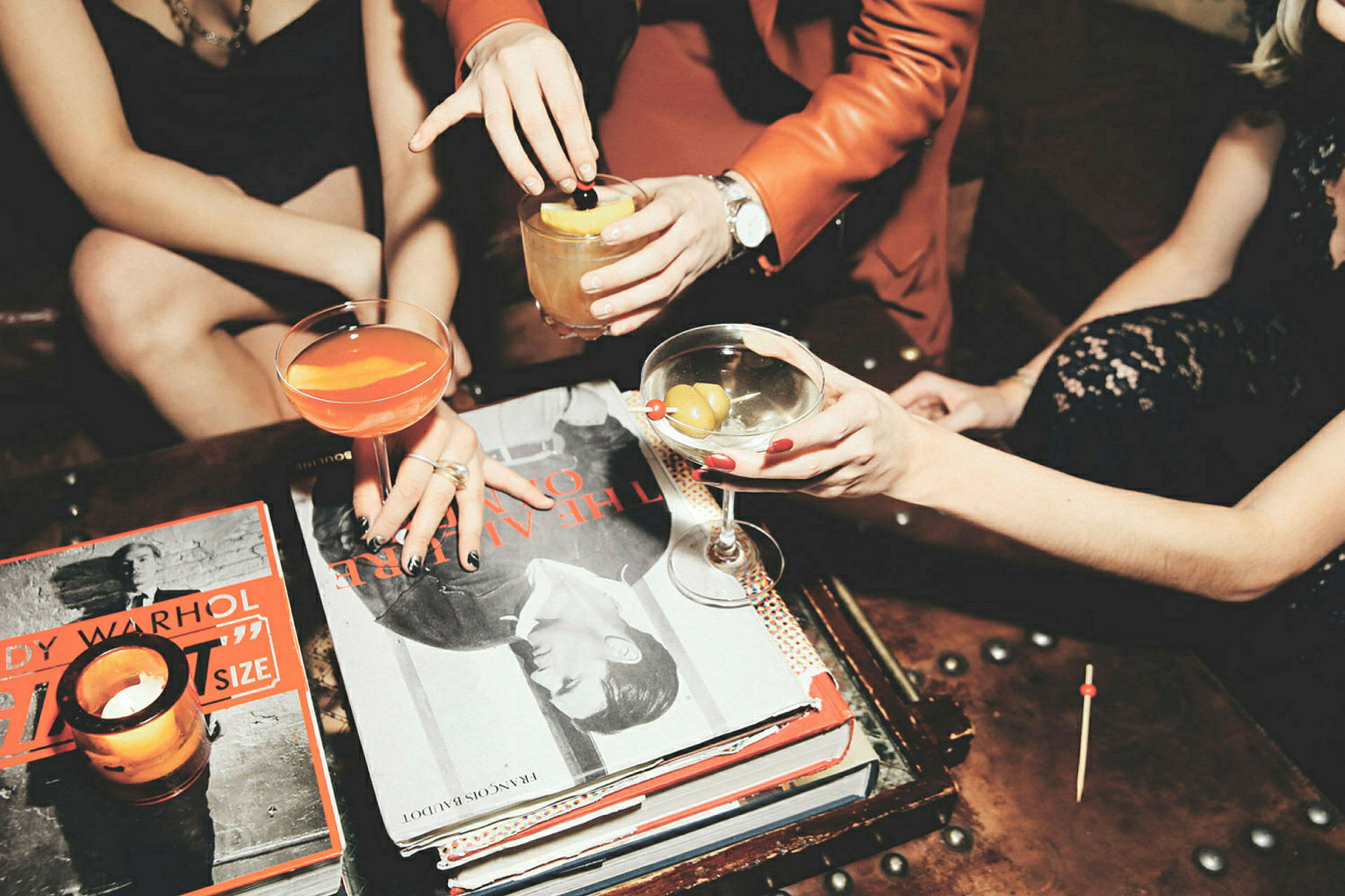 Mennesker holder og skåler med forskellige cocktails ved et bord. (AI-genereret tekst)