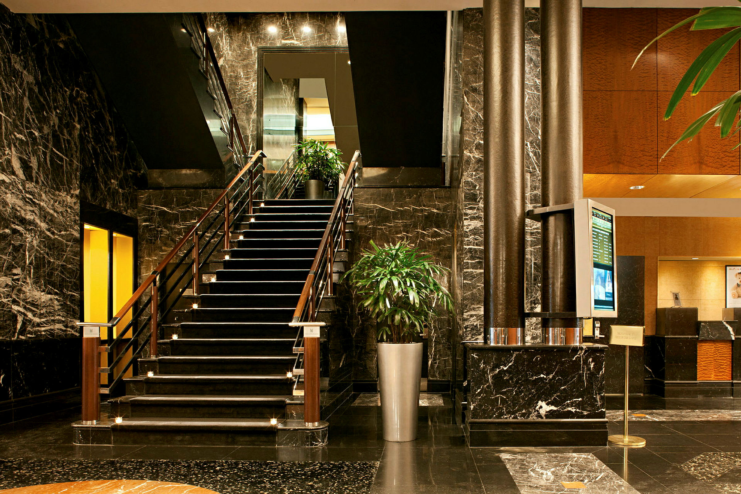 En hotellobby med en trappe, marmoverflader og grønne planter. (AI-genereret tekst)