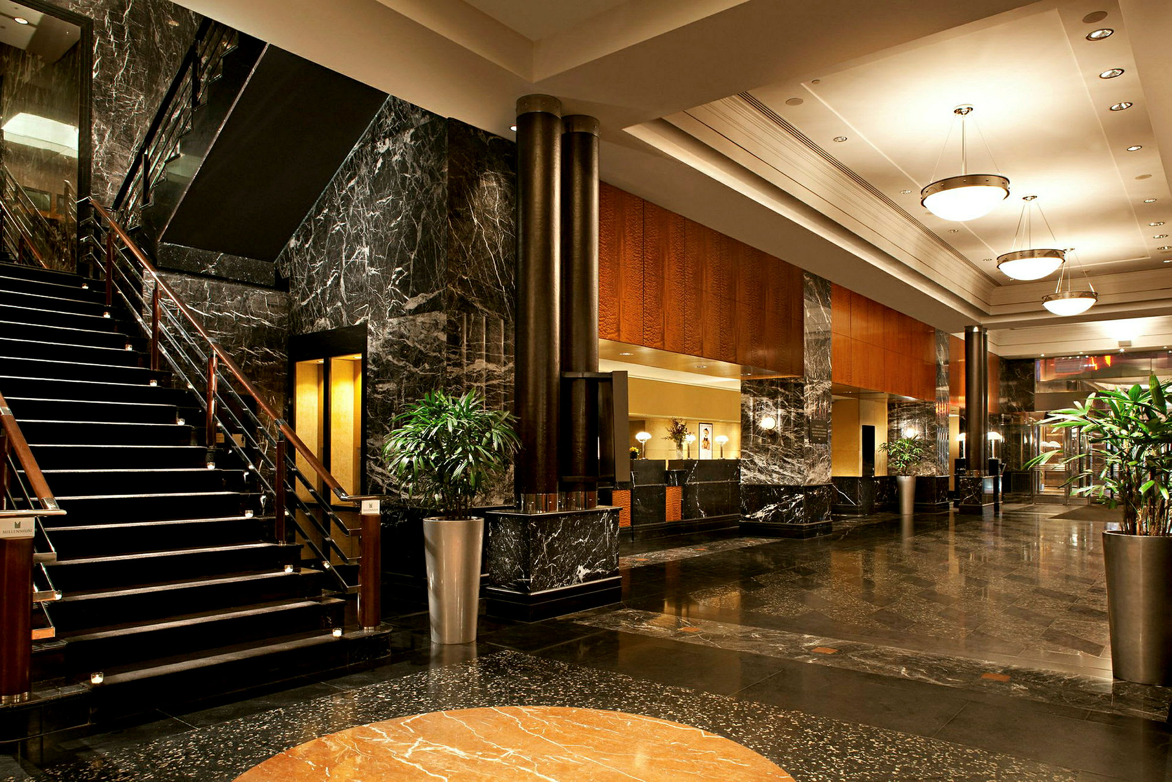 Billede af hotellets lobby med marmorgulv, en trappe, sofaer og plantearrangementer. (AI-genereret tekst)
