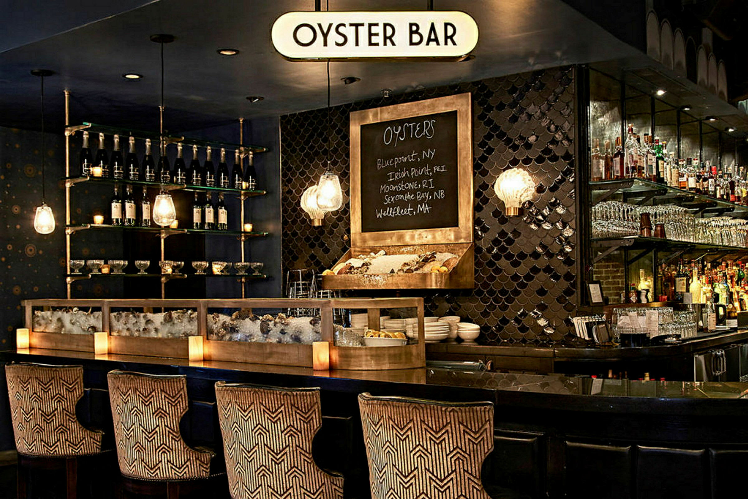 En stilfuld oysterbar med en disk fyldt med is og østers, flasker og glas på hylder samt dekorative lamper. (AI-genereret tekst)