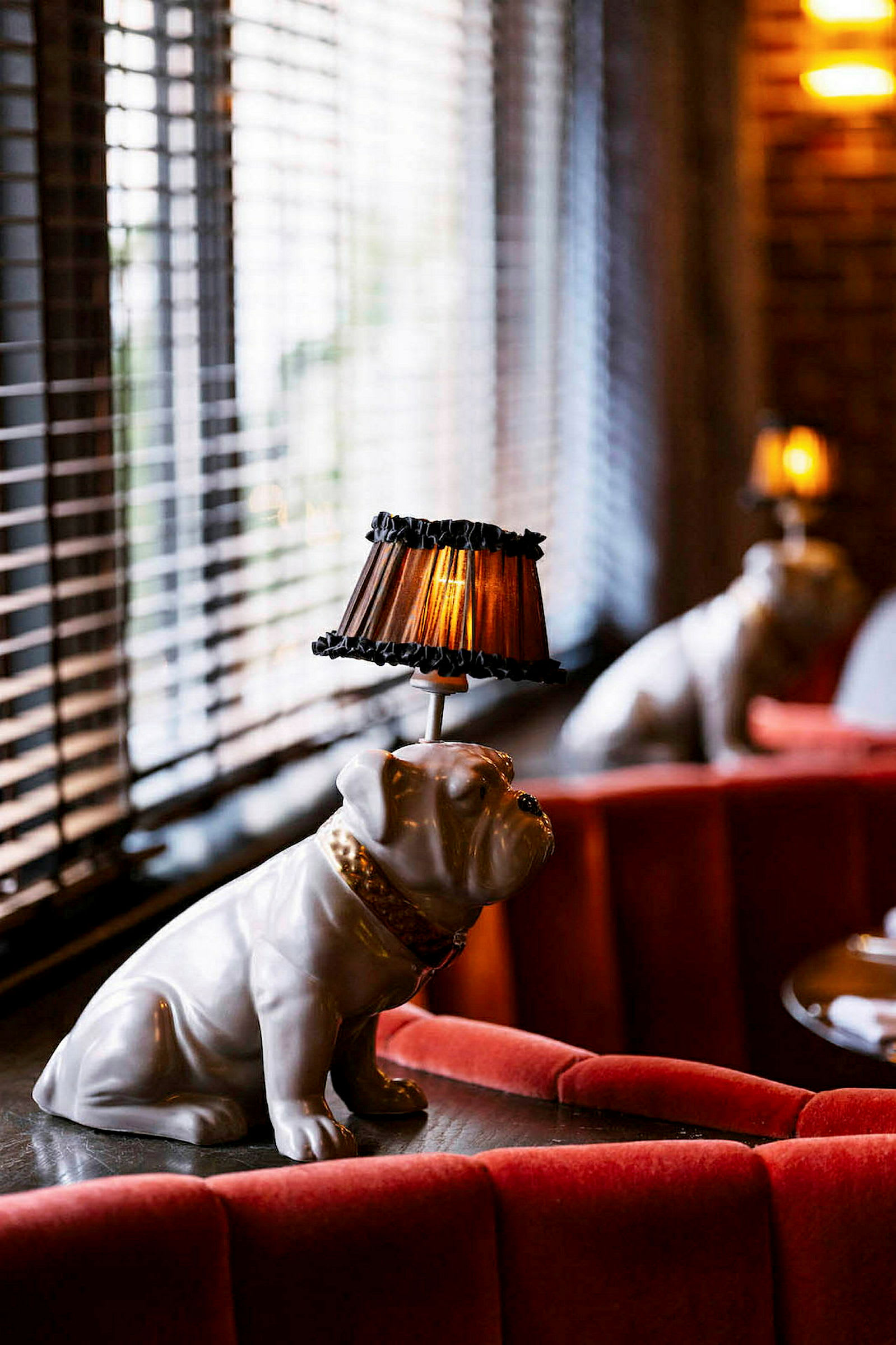 En dekorativ lampe formet som en bulldogstatue med en lampeskærm på hovedet står på et bord omgivet af røde sofaer. (AI-genereret tekst)