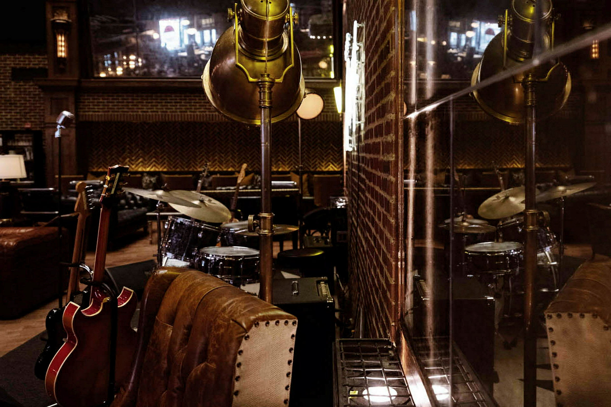 Et rum dekoreret med musikinstrumenter, herunder et trommesæt og guitarer, samt møbler og en murstensvæg. (AI-genereret tekst)