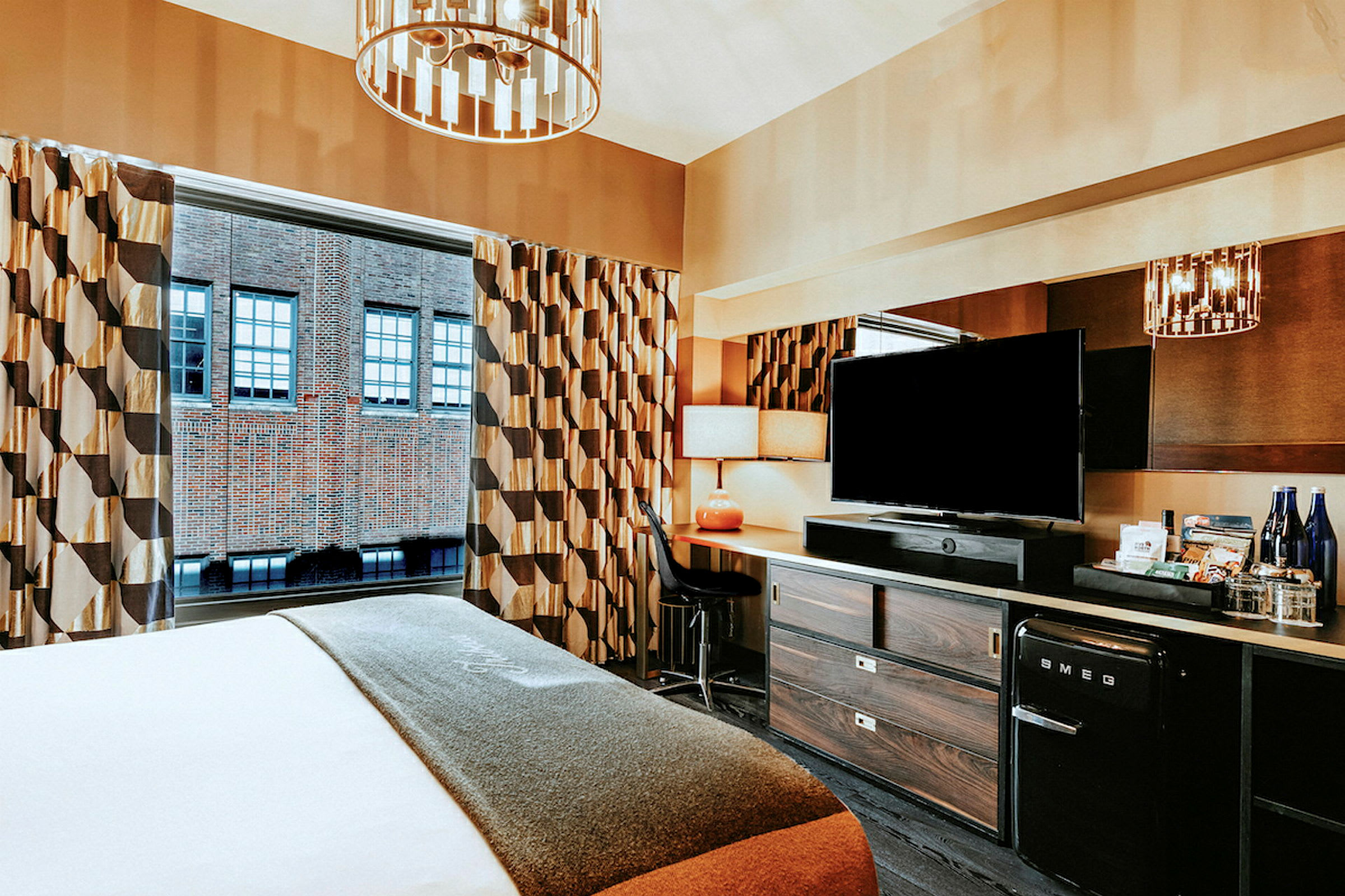 Hotelværelse med en seng, skrivebord og TV samt vindue mod en murstensbygning. (AI-genereret tekst)