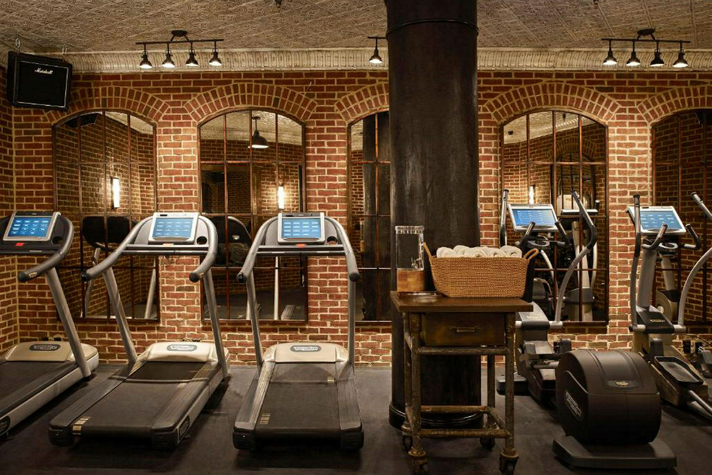Et fitnesscenter med løbebånd og træningsudstyr foran en murstensvæg. (AI-genereret tekst)