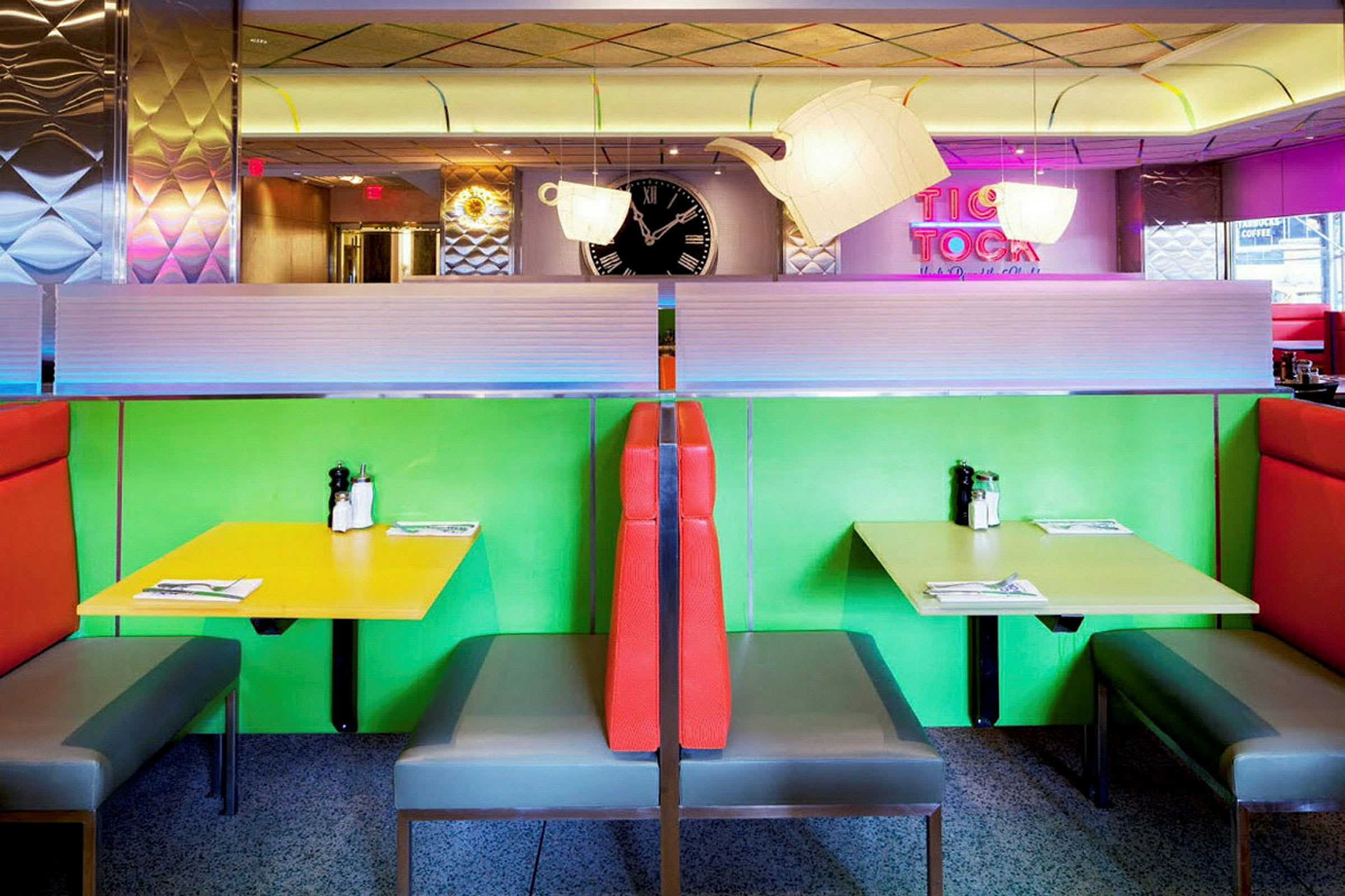 Farverige siddekabiner i en retrorestaurant med grøn og gul farve på bordene samt rød polstring på ryglænene. (AI-genereret tekst)
