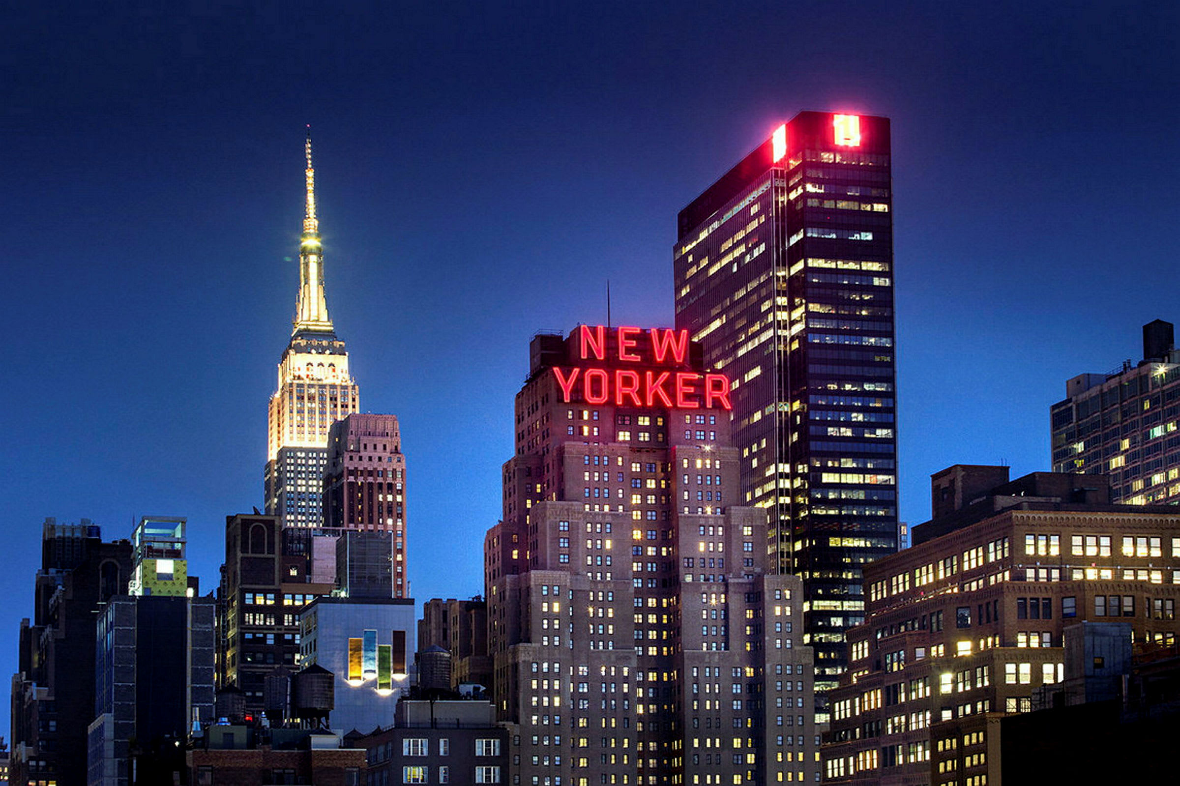 En bysilhuet med oplyste bygninger og skiltet "New Yorker" synligt mod en mørk nattehimmel. (AI-genereret tekst)