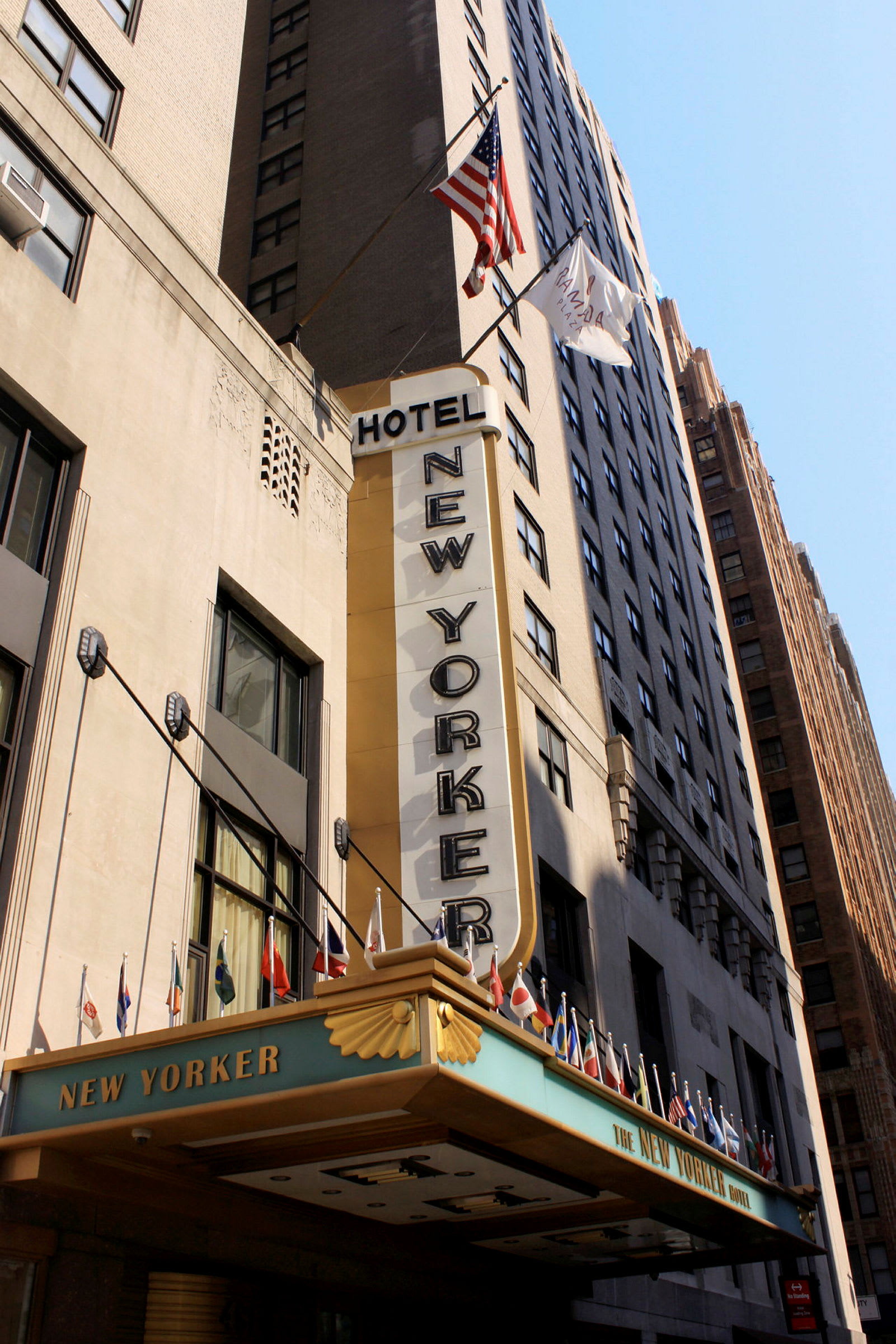 Facaden af en bygning med teksten "Hotel New Yorker" og flag der hænger fra baldakinen. (AI-genereret tekst)