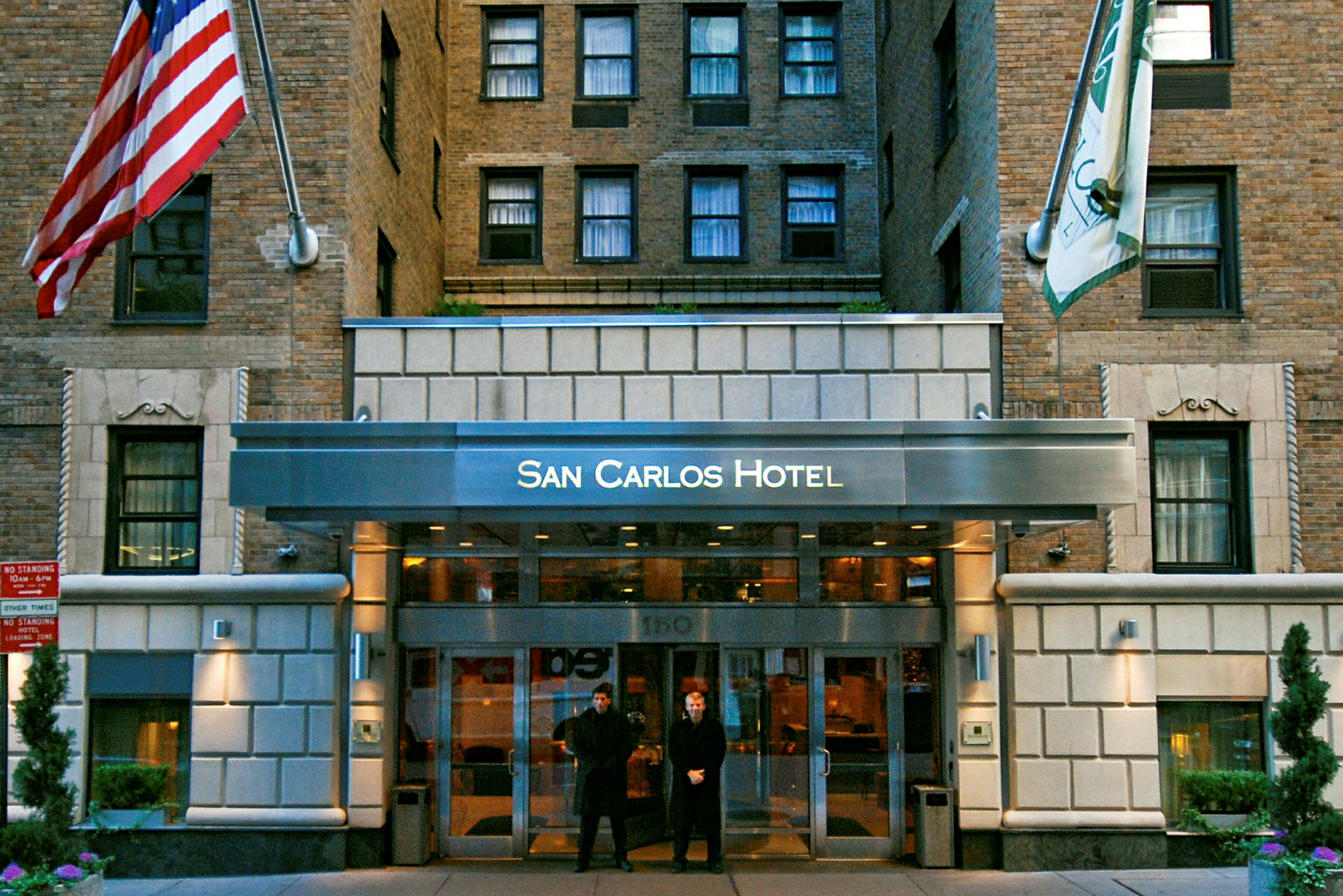 Indgangen til San Carlos Hotel, en bygning facade med mursten og flag. (AI-genereret tekst)