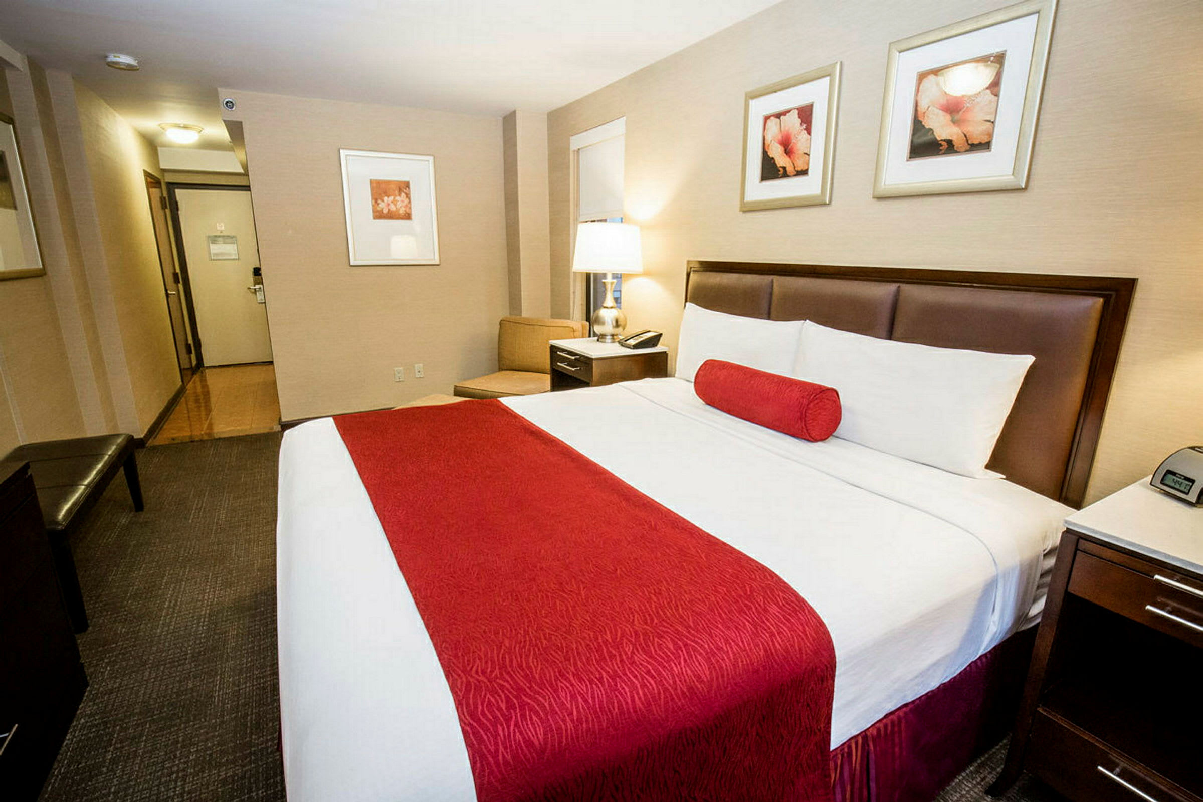 Hotelværelse med en stor seng med røde detaljer. Skrivebord og lampearmatur ved siden af. (AI-genereret tekst)